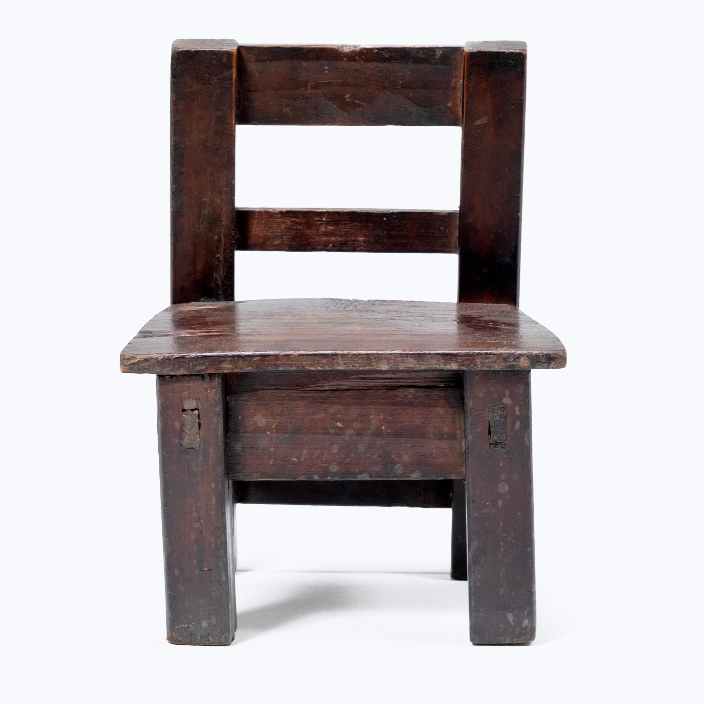 Crafted in the early 20th century, this petite Guatemalan children's chair charms with its playful asymmetry and richly textured surface. Influenced by Spanish Colonial furniture design, the angular chair has a slatted back and tapered seat resting