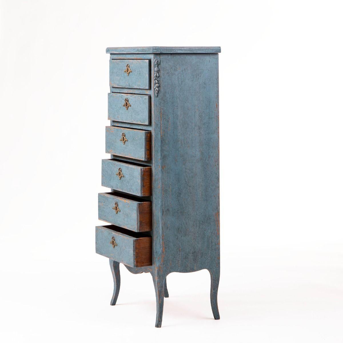 Cassapanca Wellington in stile gustaviano, realizzata in pino dipinto di blu.
Il frontale è dotato di sei cassetti con maniglie in ottone, un bordo superiore profilato e angoli inclinati ornati da ornamenti intagliati in rilievo.
La cassapanca