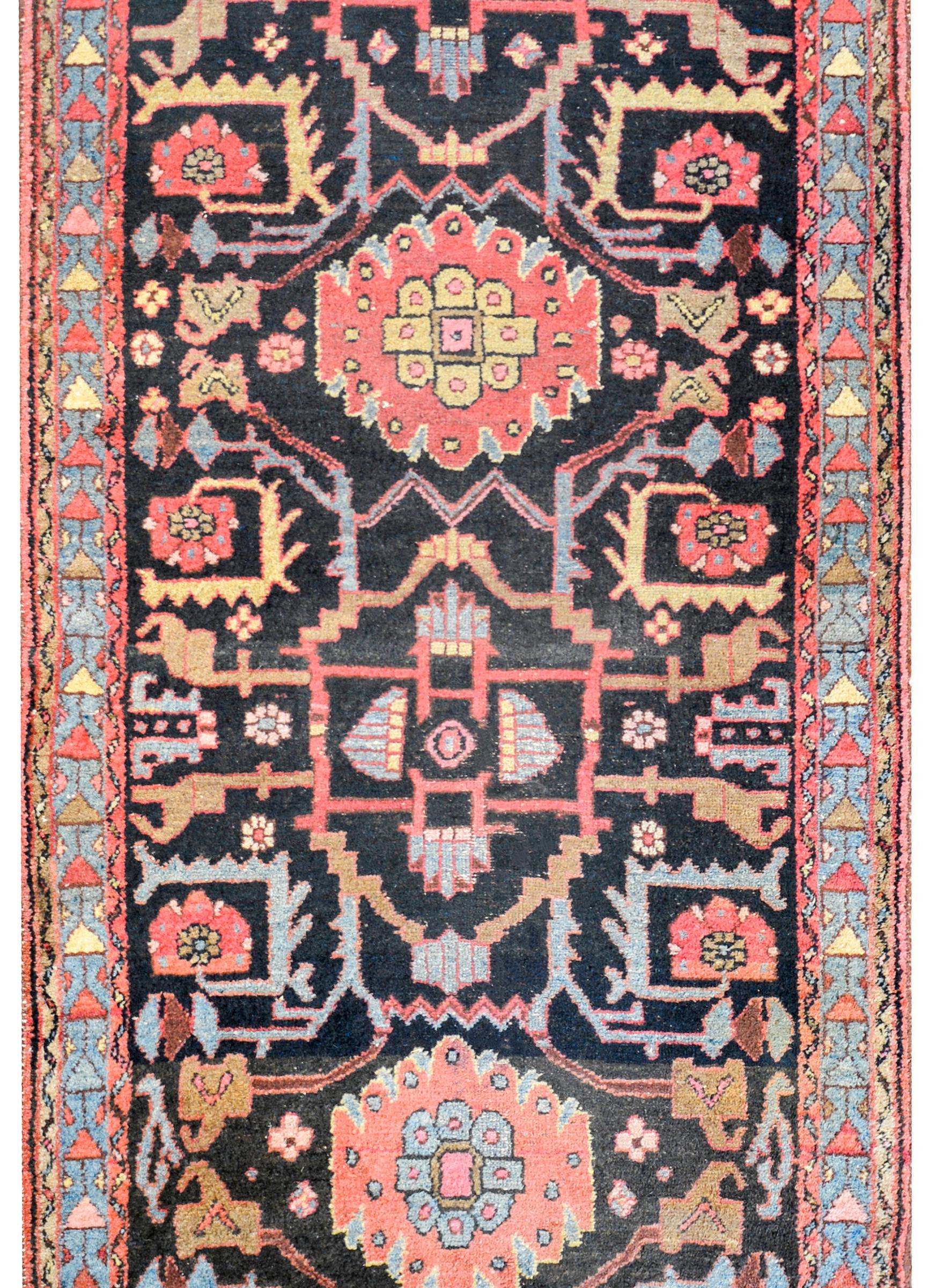 An early 20th century Persian Hamadan rug with a fantastic tribal pattern containing two large diamond floral medallions, on a black background, with stylized vine patterned motif. The border is wonderful with a triangle pattern on a light indigo