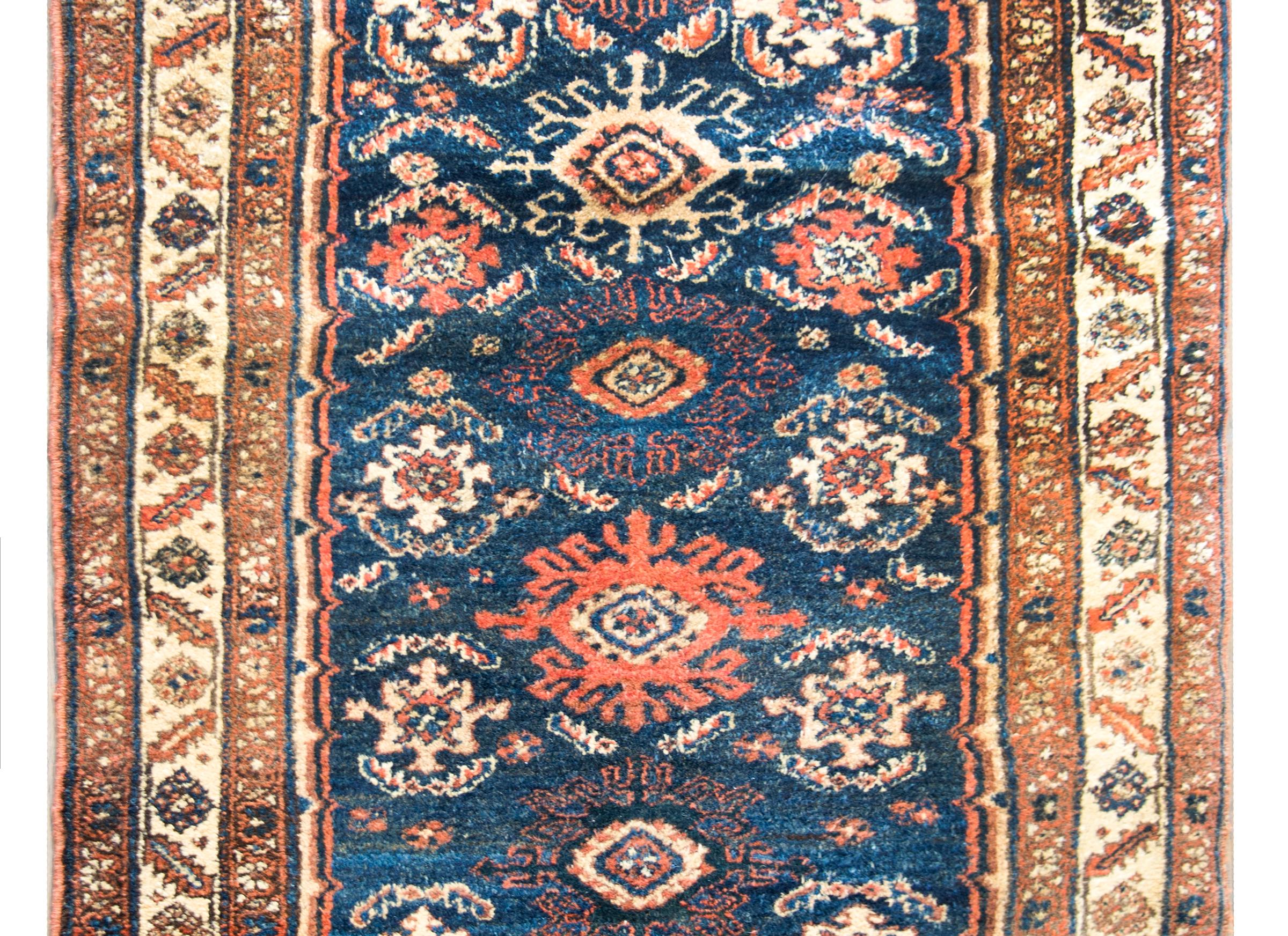 A stunning early 20th century Persian Hamadan rug with a beautiful all-over stylized floral pattern woven in crimson, indigo, cream, and gold, and set against a dark indigo background. The border is complex with multiple petite floral patterned