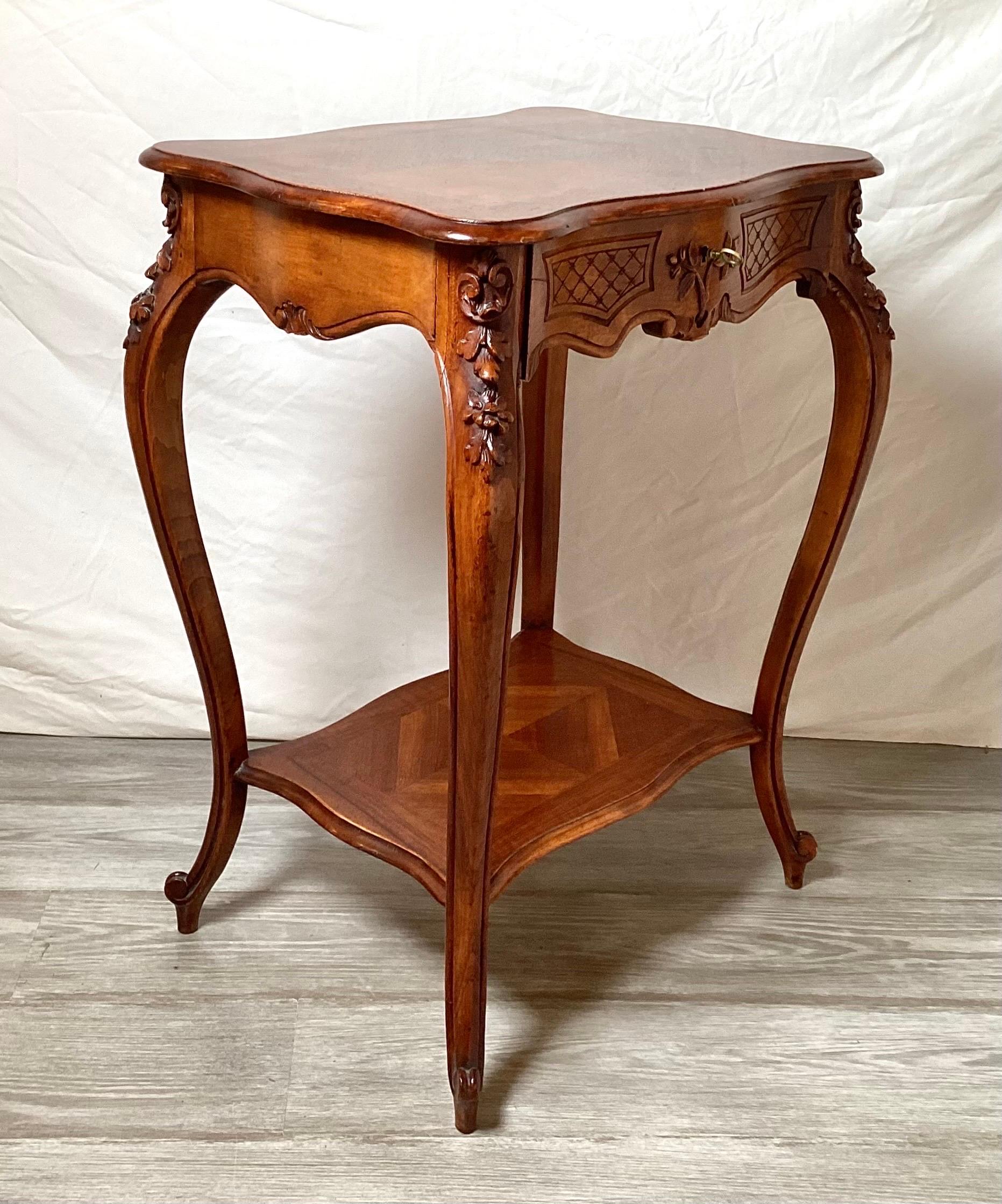 Elegant hand carved walnut side table. The shapely top with drawer with brass pull supported by four curved cabriole legs with lower shelf. The wood finish in excellent condition with a nice warm natural patination.