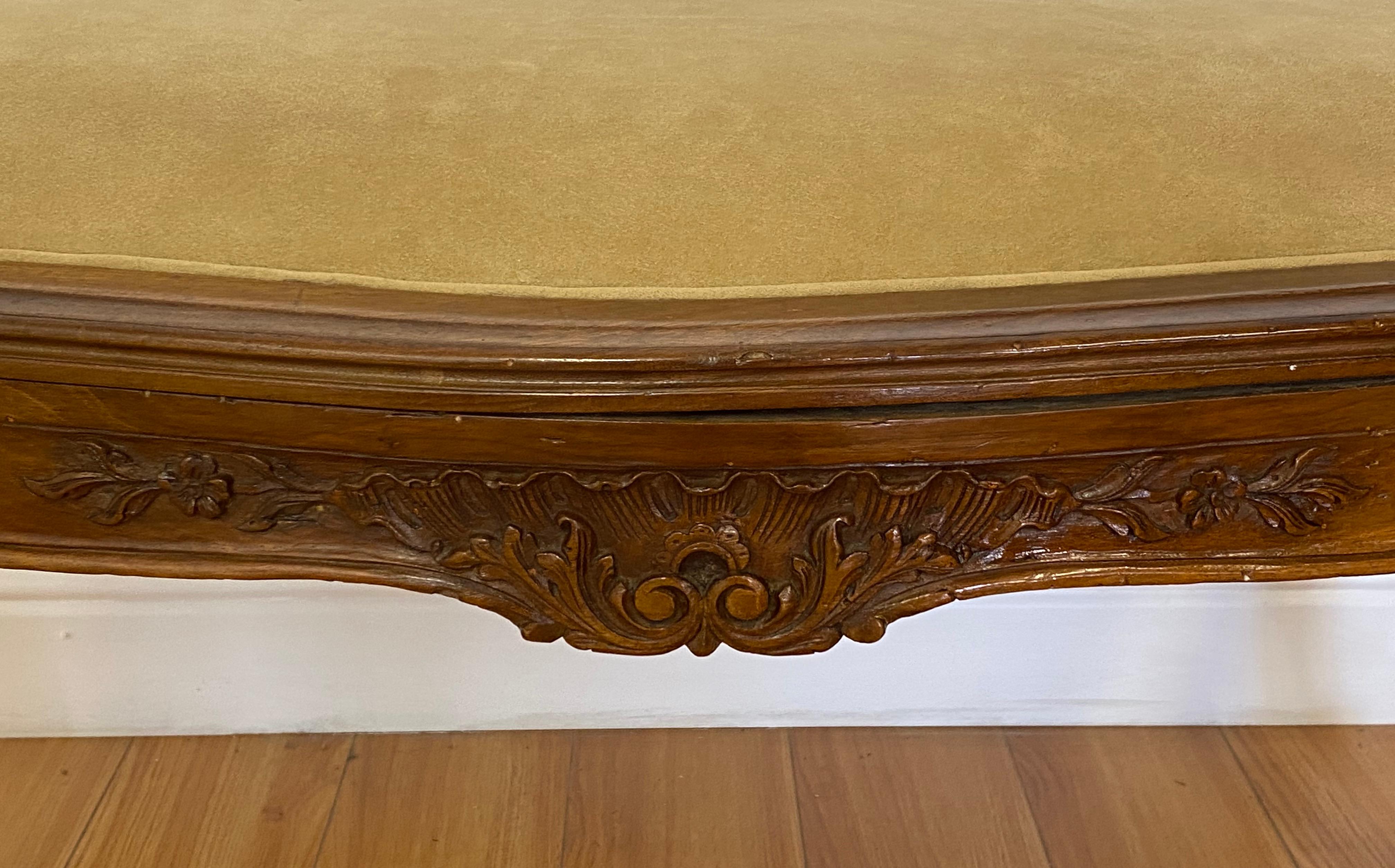 Early 20th century hand carved French walnut bench c.1900

Remnants of the original wicker seat are still visible underneath. The new seat appears to be added in the mid 20th century.

The frame shows some all around distress and some lifting at