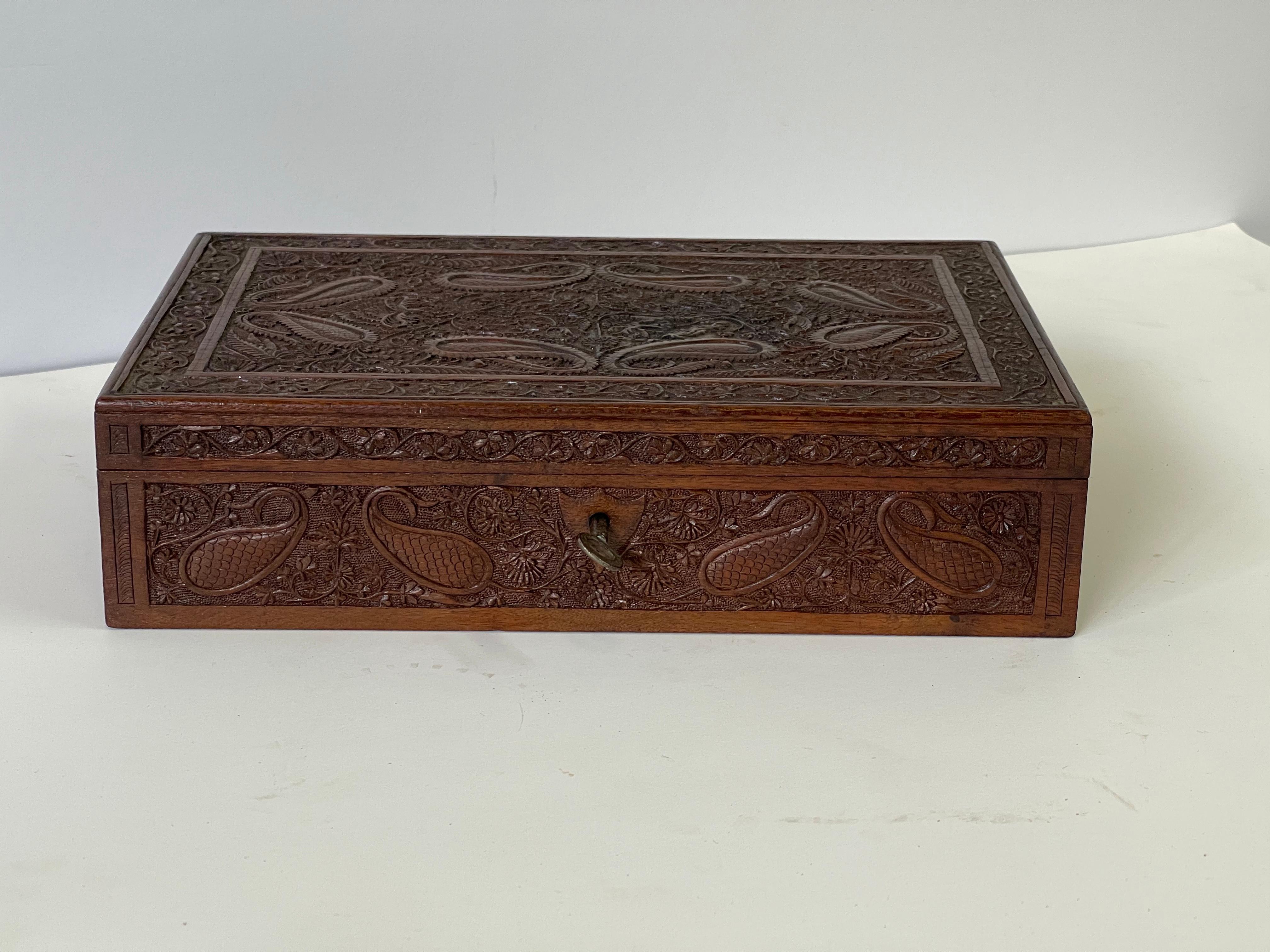 Early 20th century Anglo Raj wooden hand-carved jewelry box richly decorated overall with paisley and floral carvings. A hinged lid opens to a shallow relief carving on the interior and a divided compartment for storing valuables under the original
