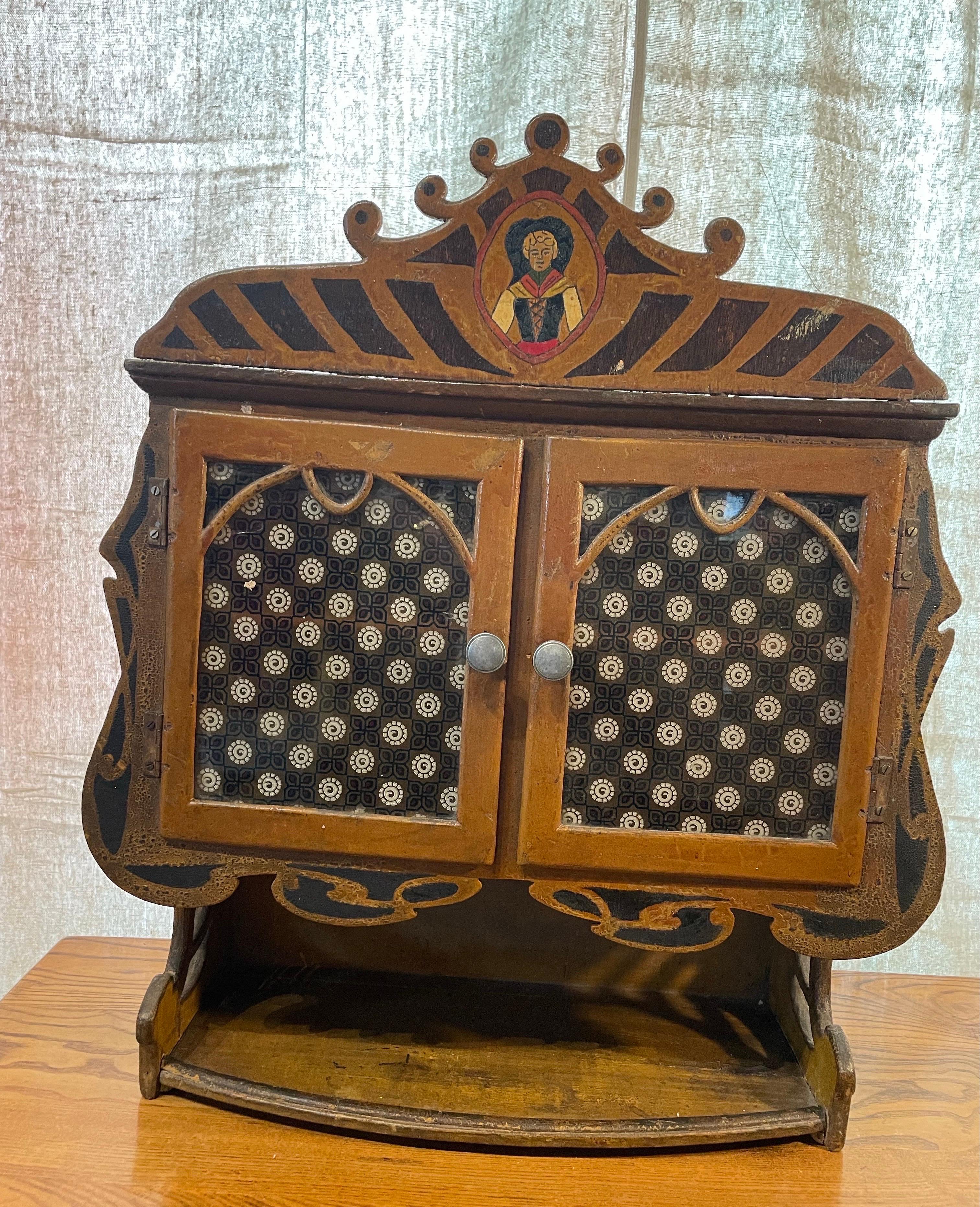 This charming hand-crafted wall cabinet, dating to the late 19th or early 20th century, is a fine example of Central European folk art—likely originating from Hungary or the Transylvanian region. Crafted from wood and retaining its original