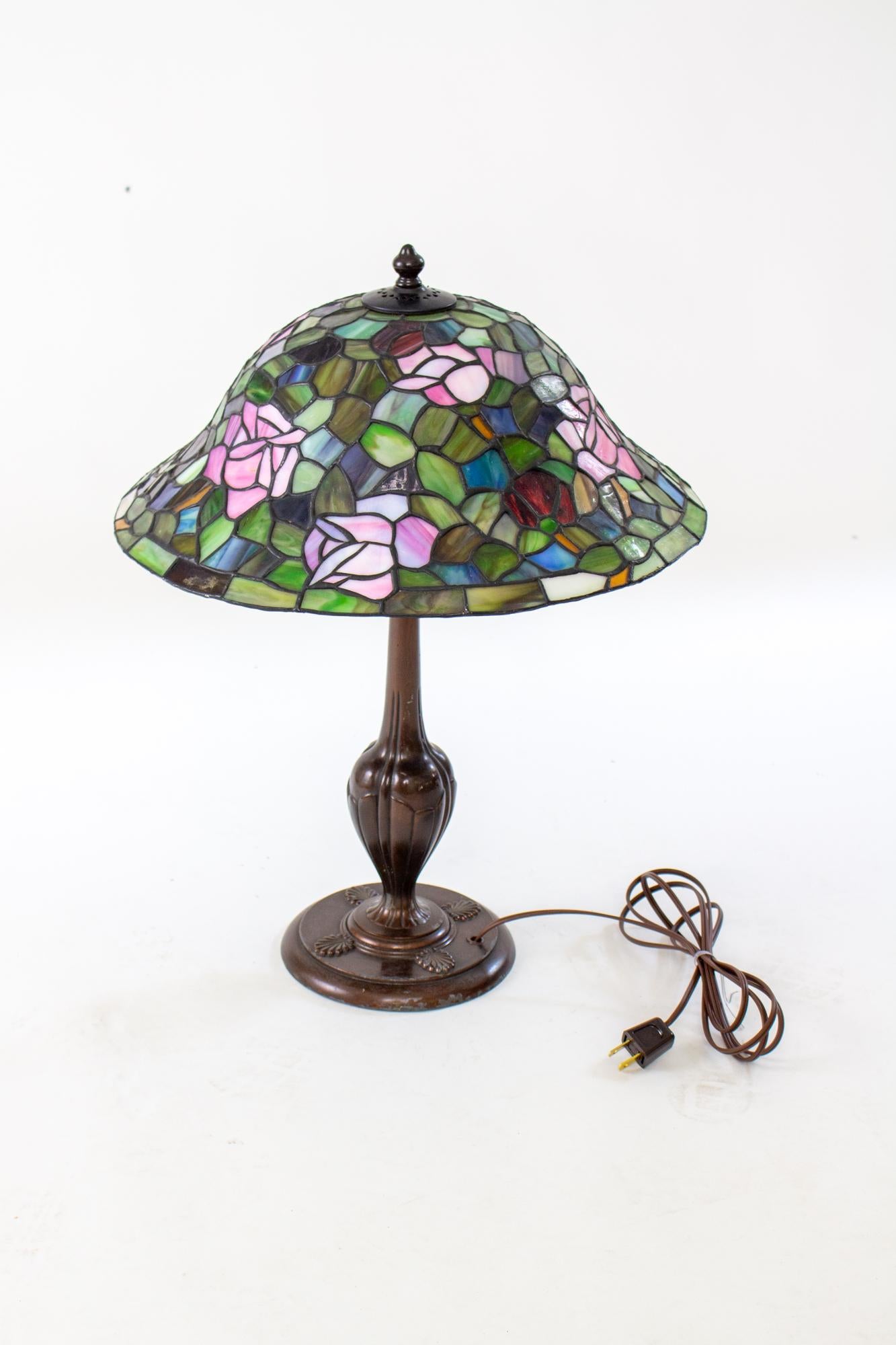 Early 20th century table lamp, attributed to Handel. Round Base in cast metal with a dark bronze finish. Distinctive round Handle style two light cluster. Shade is late 20th Century stained glass with a rose pattern. 

Condition: Original painted