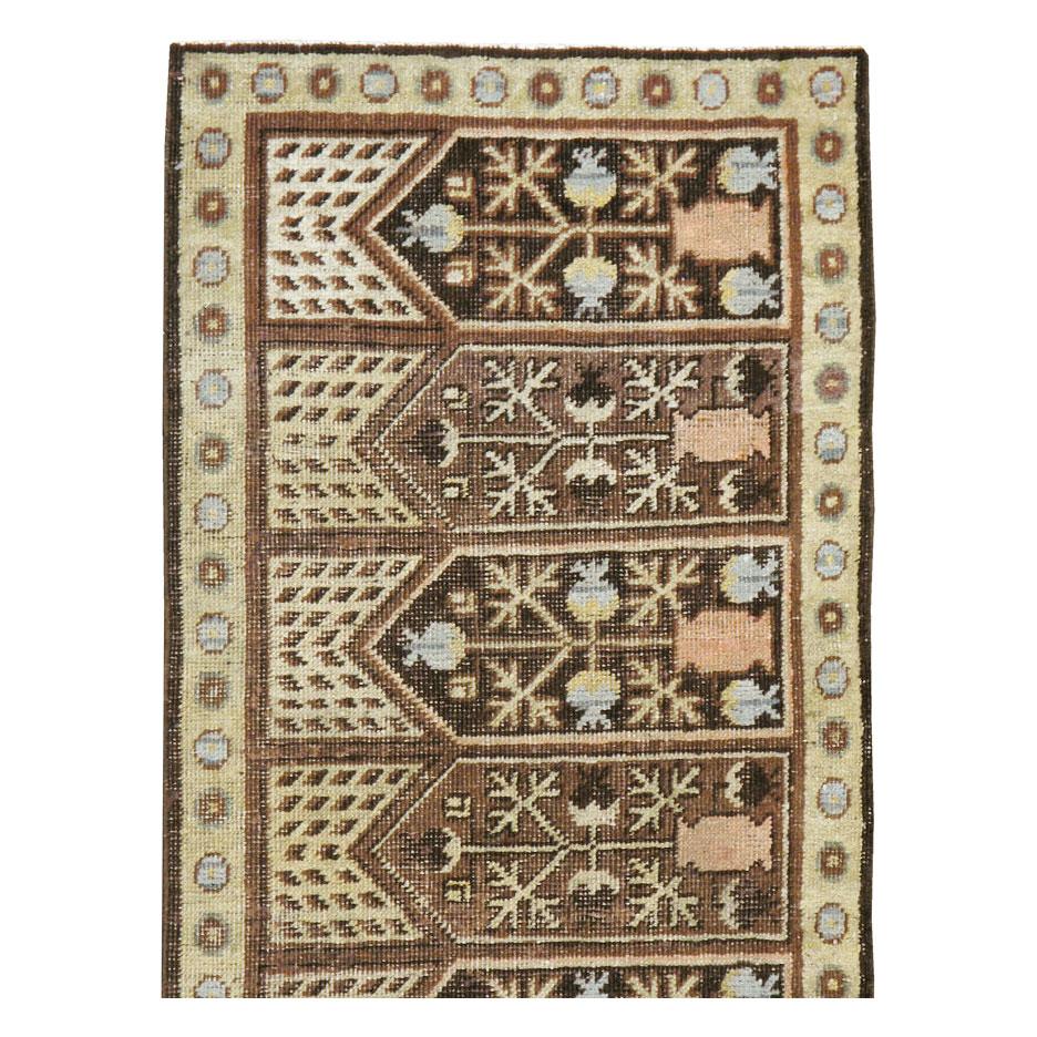 An antique East Turkestan Khotan rug handmade during the early 20th century in runner size format. Each of the 11 niches alternate from dark and light brown and consist of the classic pomegranate tree and vase design. Ivory polka dot spandrels