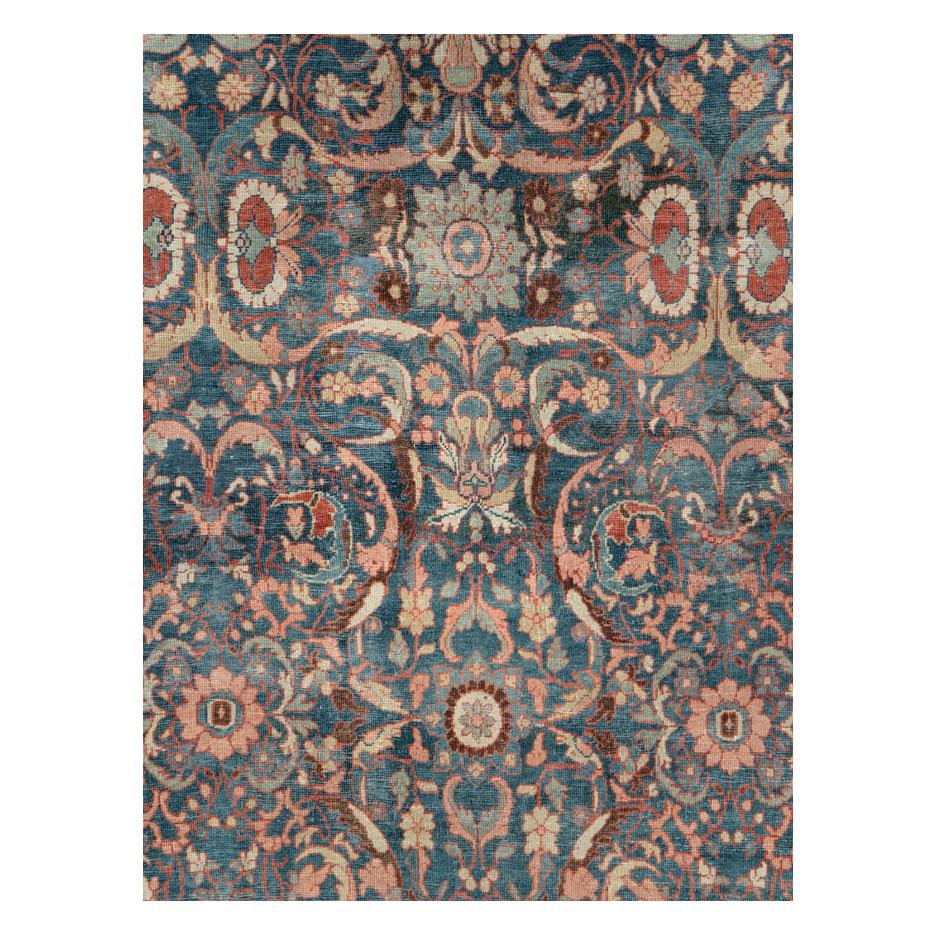 An antique Persian Mahal room size carpet handmade during the early 20th century. A reversing 'turtle palmette' border in red encloses a blue field decorated by an angular floral design in shades including blush, ivory, straw, rust red, and