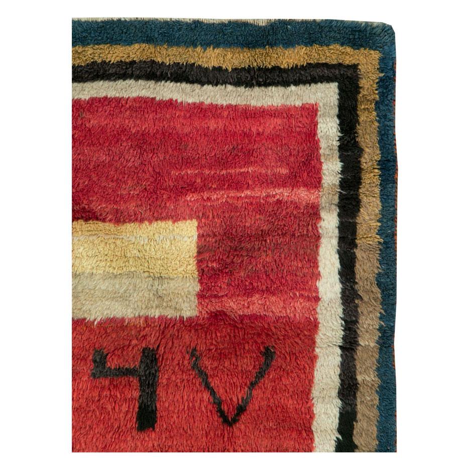 A handmade Persian Gabbeh square scatter rug with a crimson red field boldly dating 1367, (circa 1950). This tribal rug hand knotted by the nomadic Qashqai group of Persia were decades ahead of modern movements. Although totally folk and genuine by
