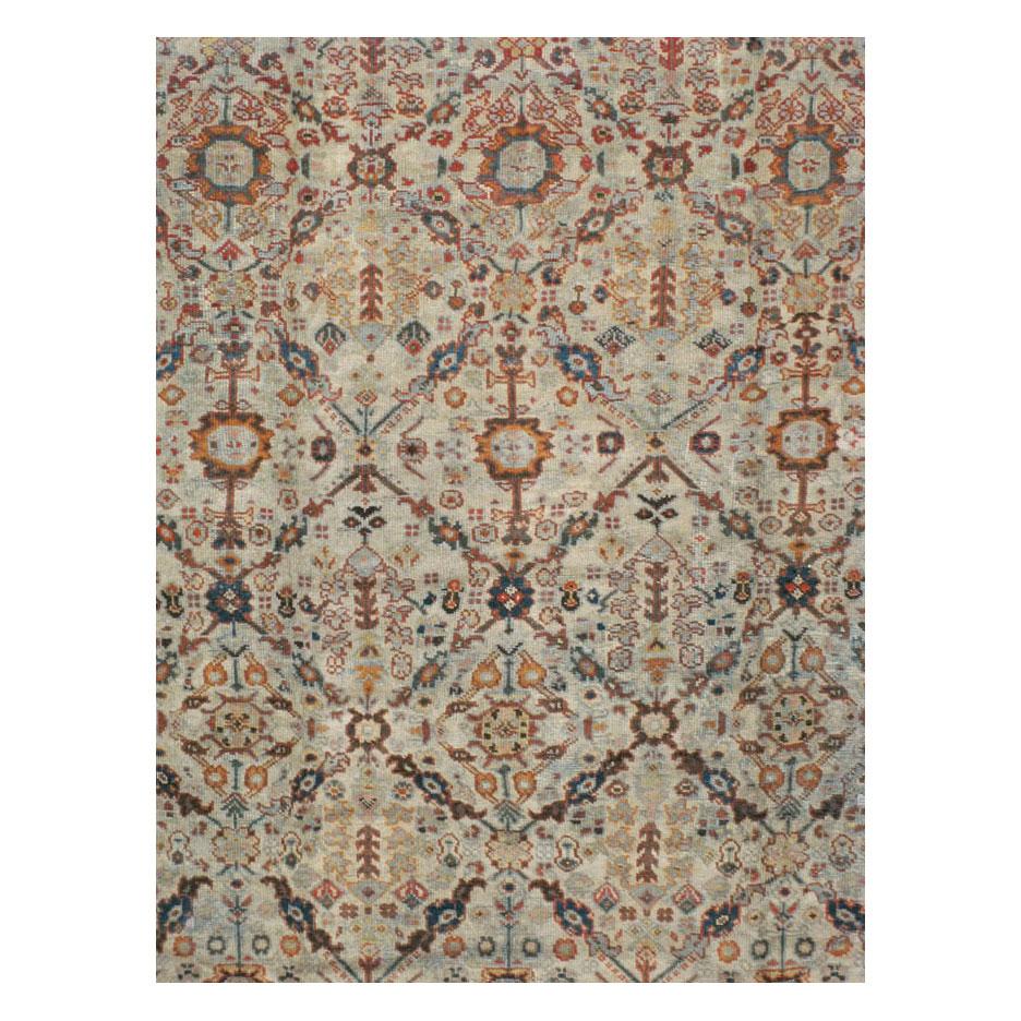 An antique Persian Mahal room size area rug handmade during the early 20th century with a diamond lattice pattern consisting of floral elements in several shades including blue and green over a light grey and beige background and a rust-red 'turtle