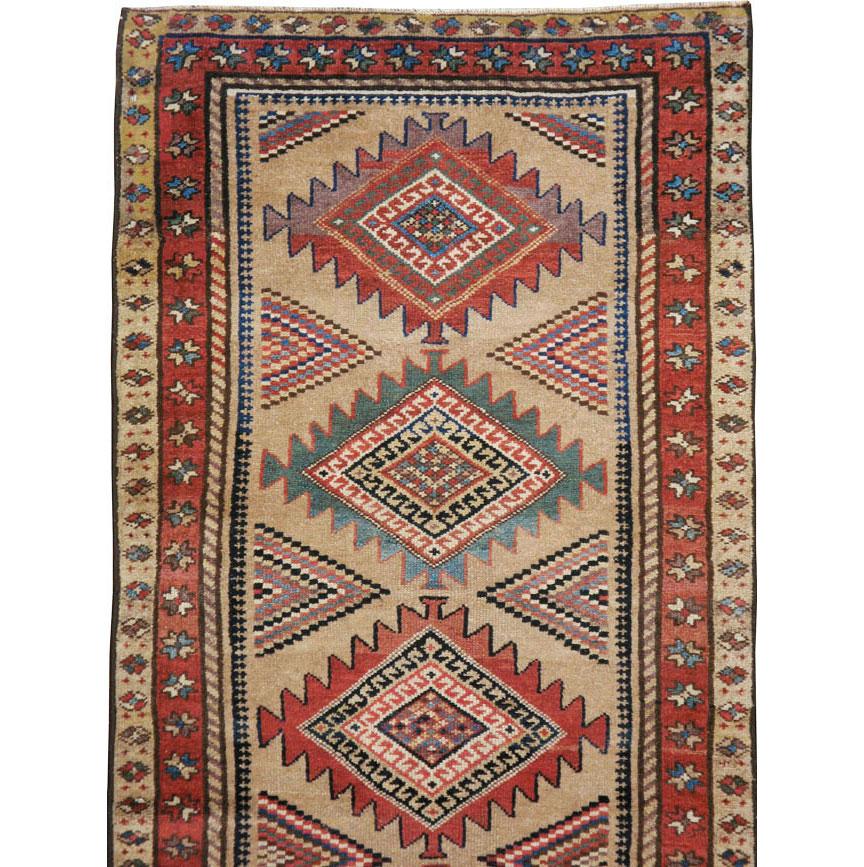 An antique Persian Serab runner from the early 20th century. The light camel brown colored field employs twelve sawtooth lozenge medallions, with no two color patterns matching, and with similarly diverse triangle side fillers. This village runner