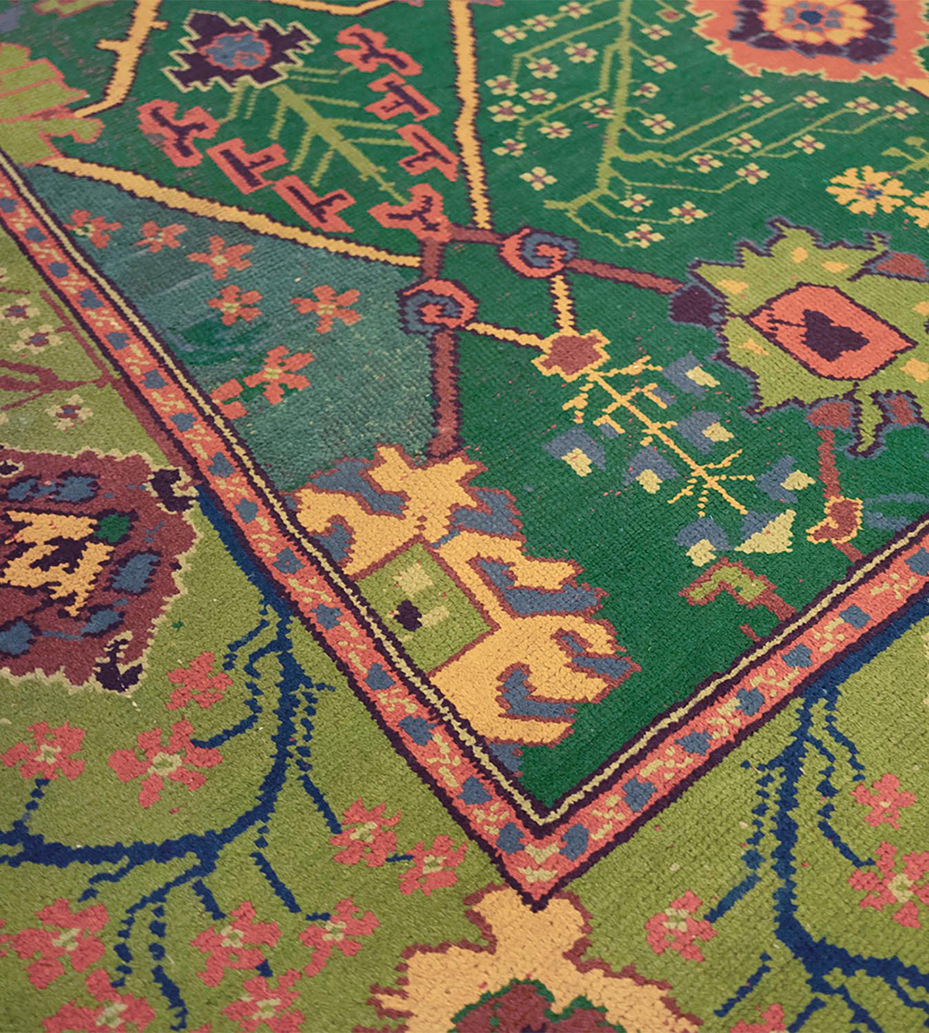 This traditional hand-woven Irish Donegal rug has a shaded bottle-green field with a counterposed design of angular vines issuing palmettes and open palmettes enclosing multiple flowering plants, in a light green border of delicate radiating