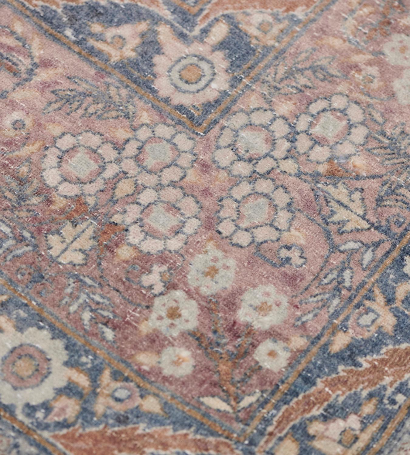 This antique Kirman Rug has a shaded blue-grey field with an overall design of polychrome palmette and serrated leaf vine, in a broad shaded light burgundy border of dense floral sprays and delicate scrolling floral vine between shaded blue floral