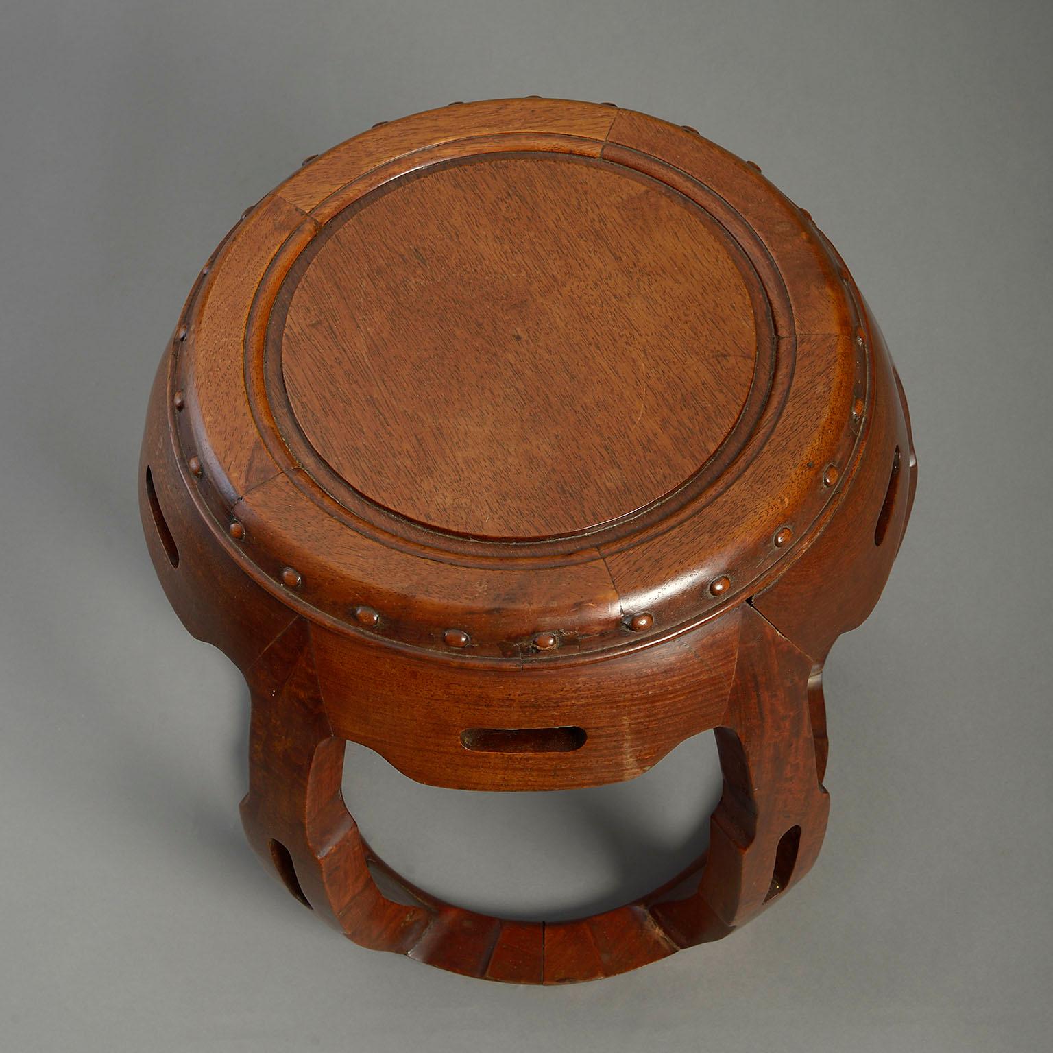 An early 20th century hardwood stool or low table of barrel form, the circular top upon pierced upright supports and set upon a ring base.