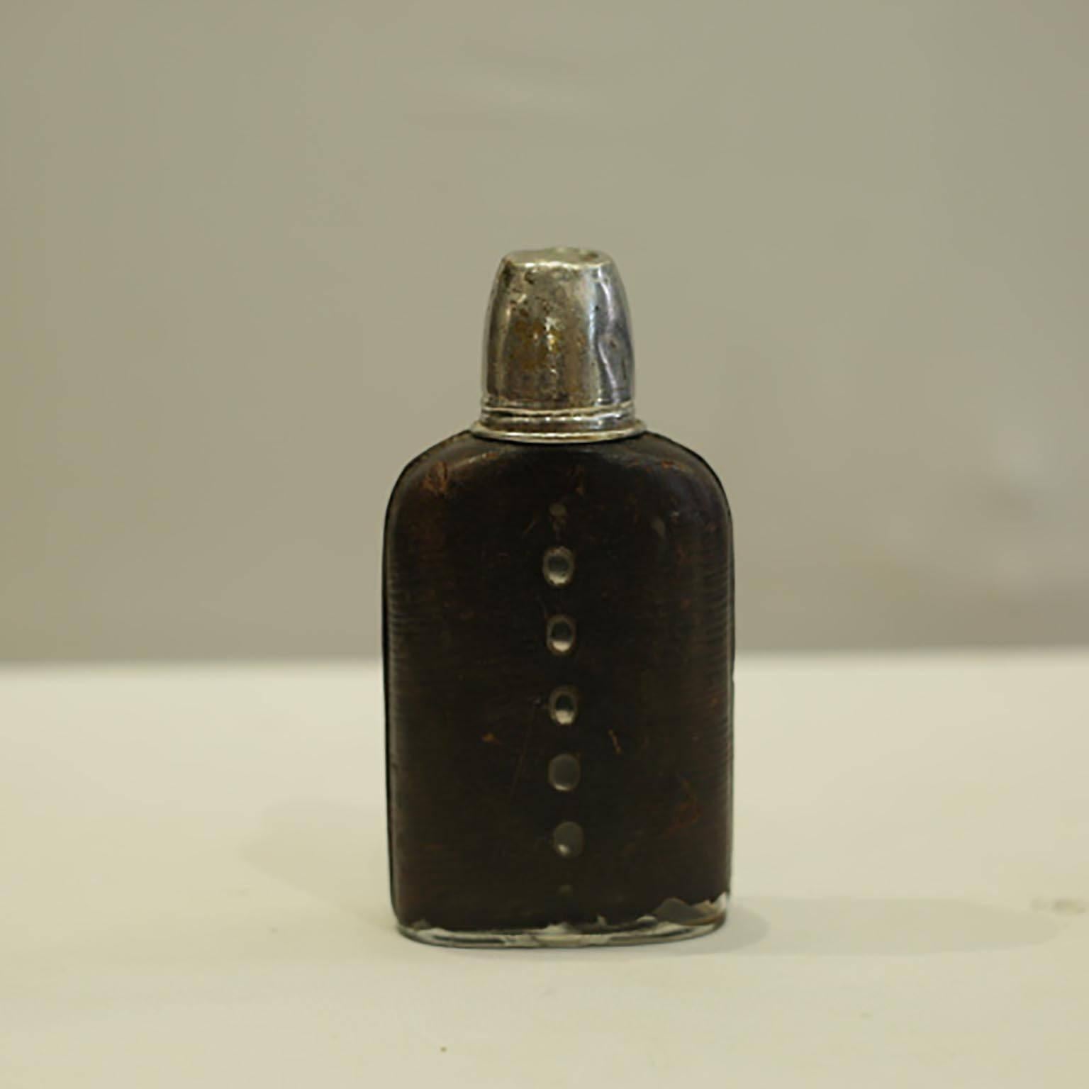 Heavy glass flask wrapped in distressed leather with perforation on both sides to see the liquor inside. The silver plated cup screws onto the flask.