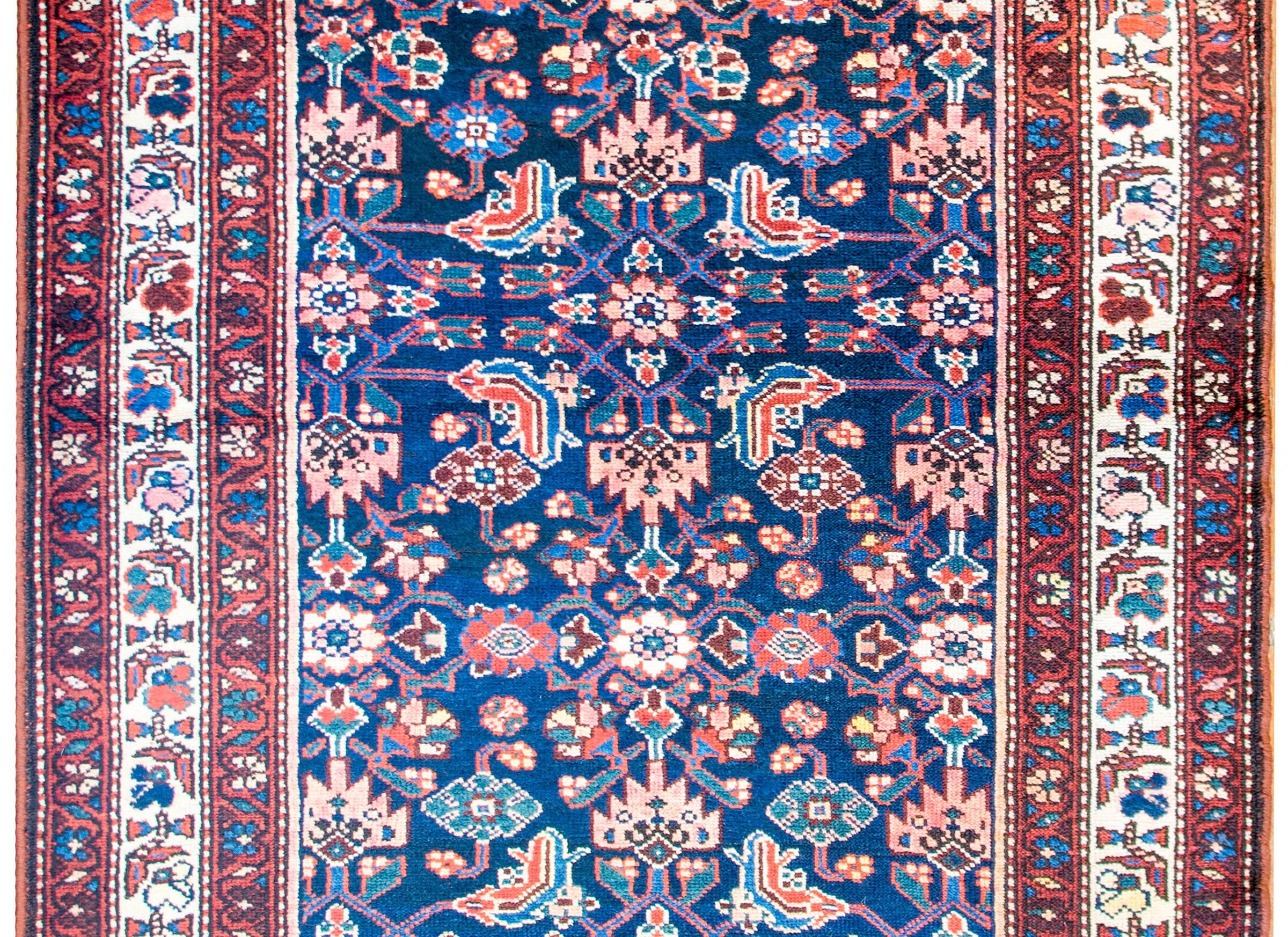 A wonderful early-20th century Persian Herati Hamadan rug with an all-over mirrored trellis pattern of flowers and vines, woven in crimson, pink, light indigo, and white colored wool, on a dark indigo background. The border is complex with a