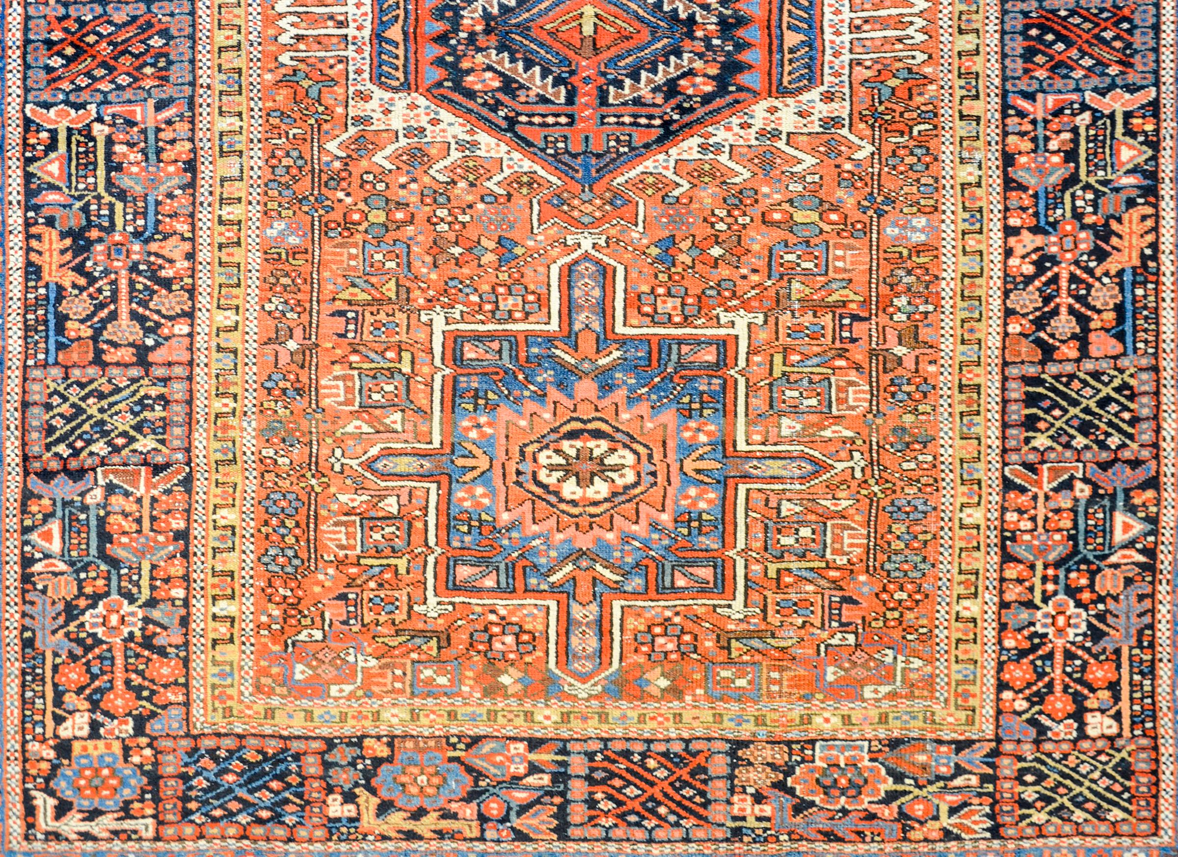 A fantastic early 20th century Persian Heriz rug with a traditional pattern of three large geometric medallions on an elaborate field of stylized flowers, leaves, and twisting vines, all woven in crimson, light and dark indigo, white, gold, black