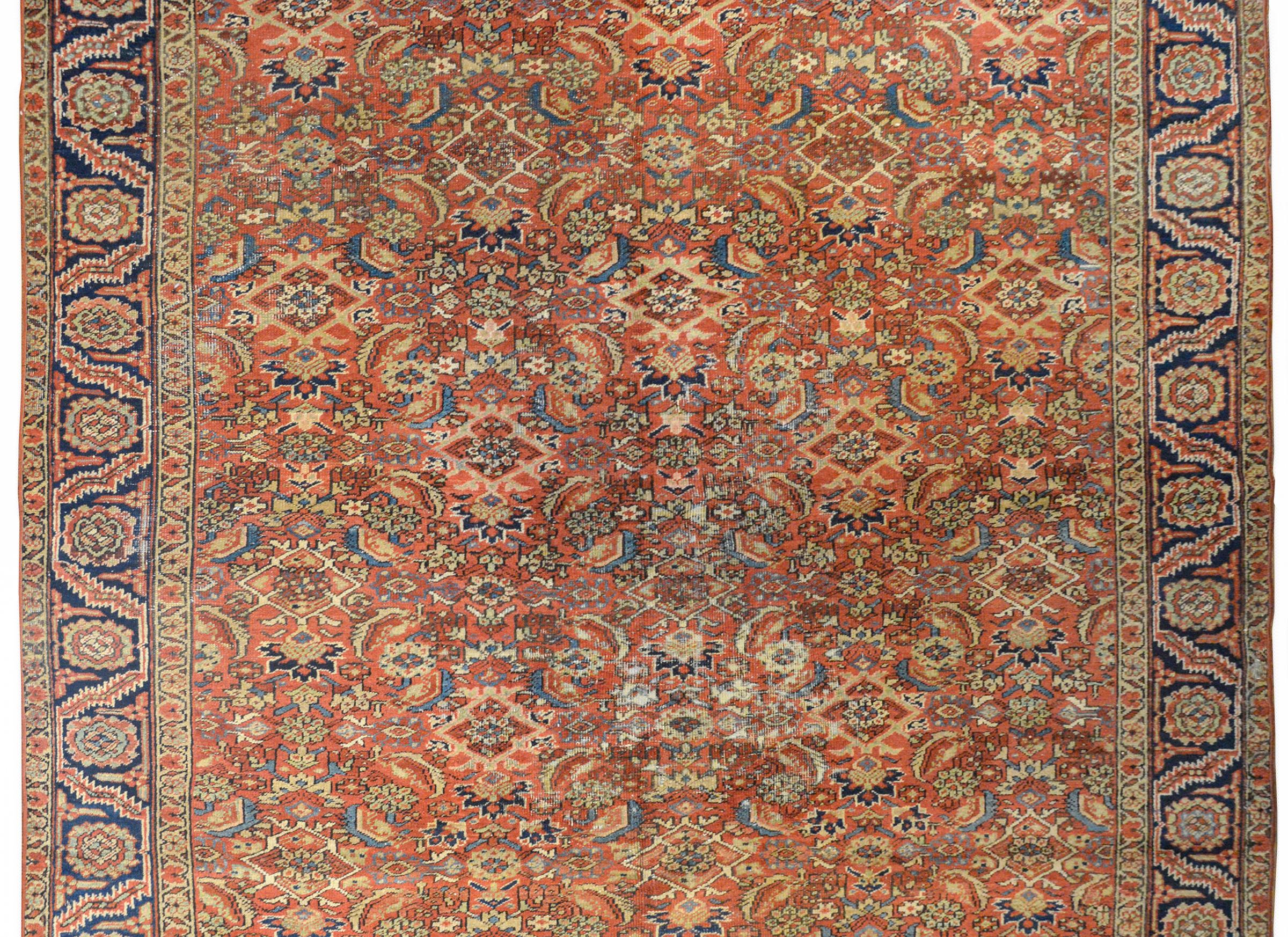 A beautiful early 20th century Persian Heriz rug with an all-over repeated floral pattern woven in light and dark indigo, cream, and pink colors on a coral colored background. The border is wonderful with a repeated large-scale floral and leaf