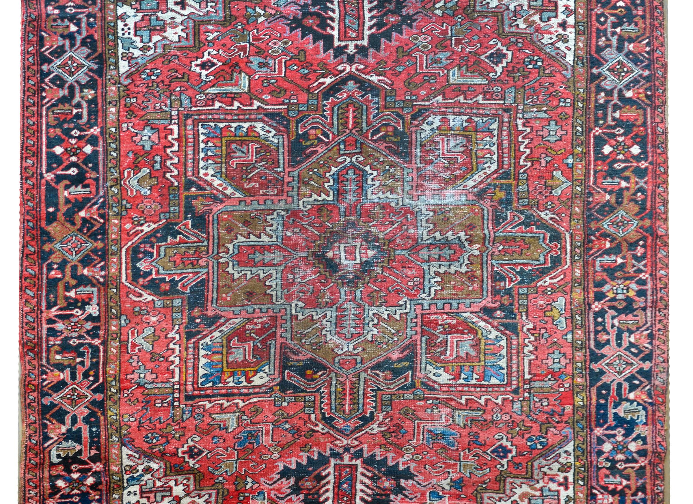 A wonderful early 20th century Persian Heriz rug with a traditional central large-scale floral patterned medallion amidst a field of more stylized flowers all woven in myriad colors including indigo, crimson, brown, and pink, and all surrounded by a