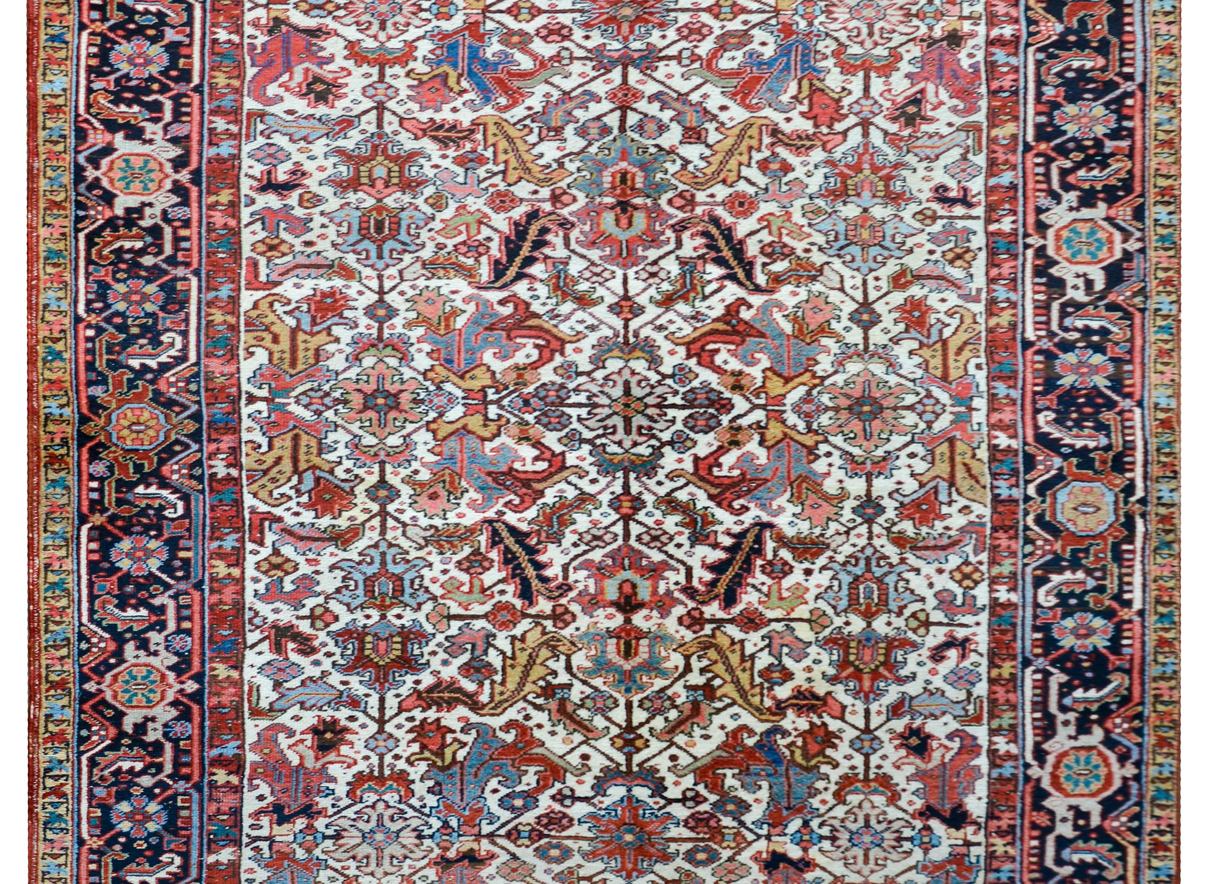 A beautiful early 20th century Persian Heriz rug a fantastic mirrored floral pattern with large-scale leaves and flowers, all woven in myriad colors including crimson, pink, gold, light and dark indigo, all against a white background. The border is