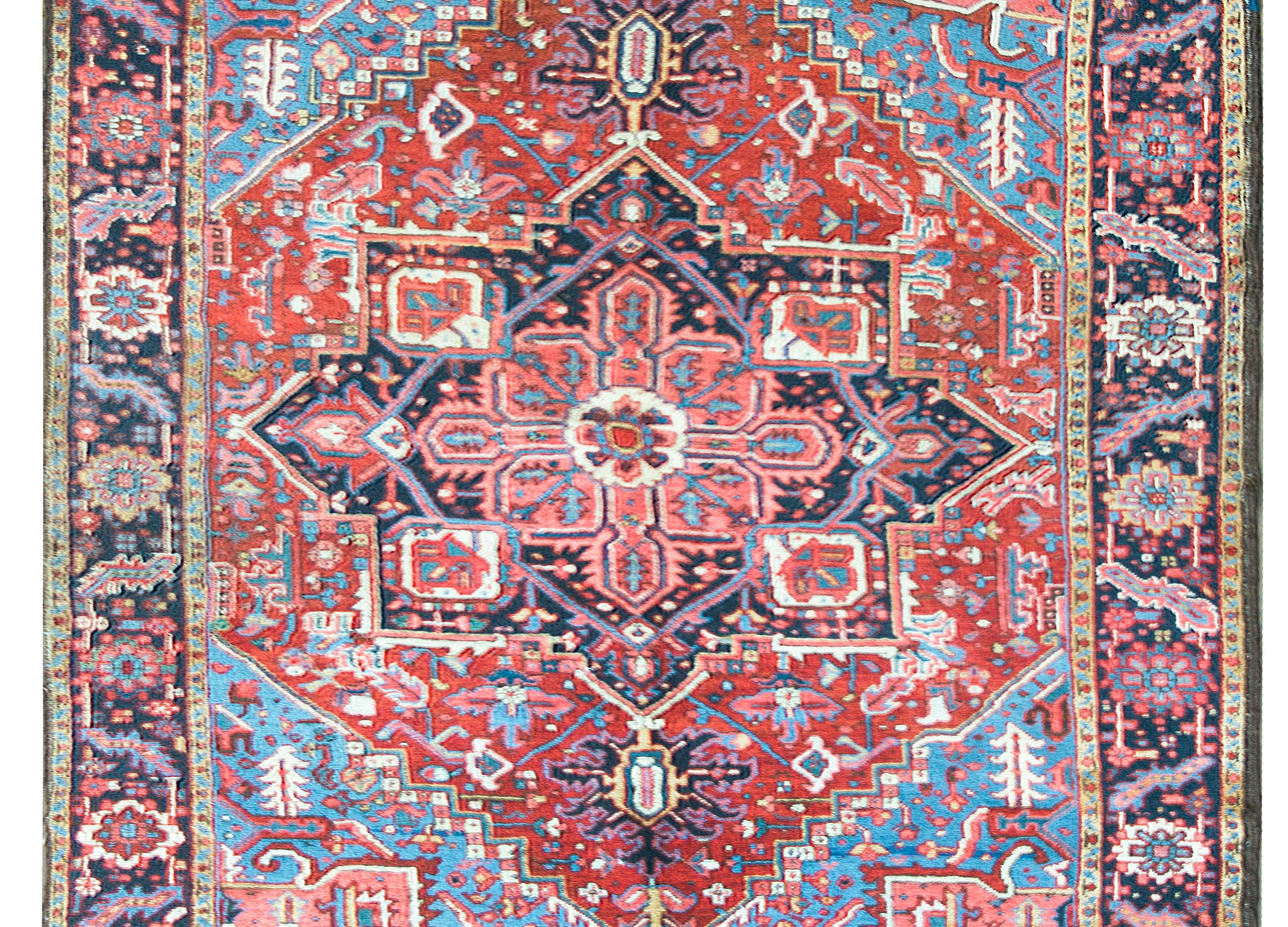 A wonderful early 20th century Persian Heriz rug with a traditional large-scale central floral medallion living amidst a field of more stylized flowers and vines, and surrounded by a wide border with a repeated large-scale floral pattern, and all