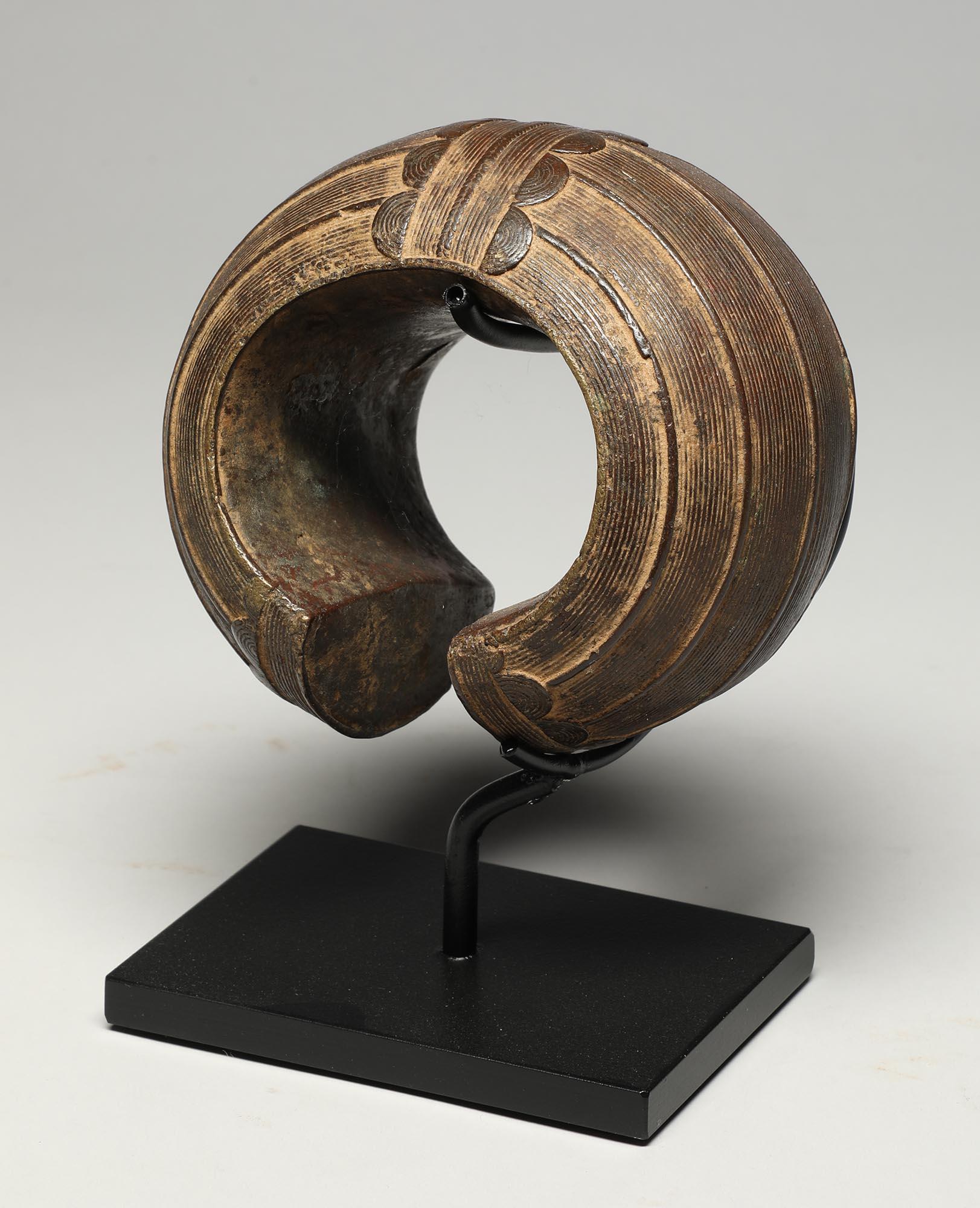 An early 20th century hollow cast bronze bracelet from the Baule of Cote d'Ivoire. Beautiful cast geometric design around outside, smooth from wear inside. On custom metal base, 5 inches high.