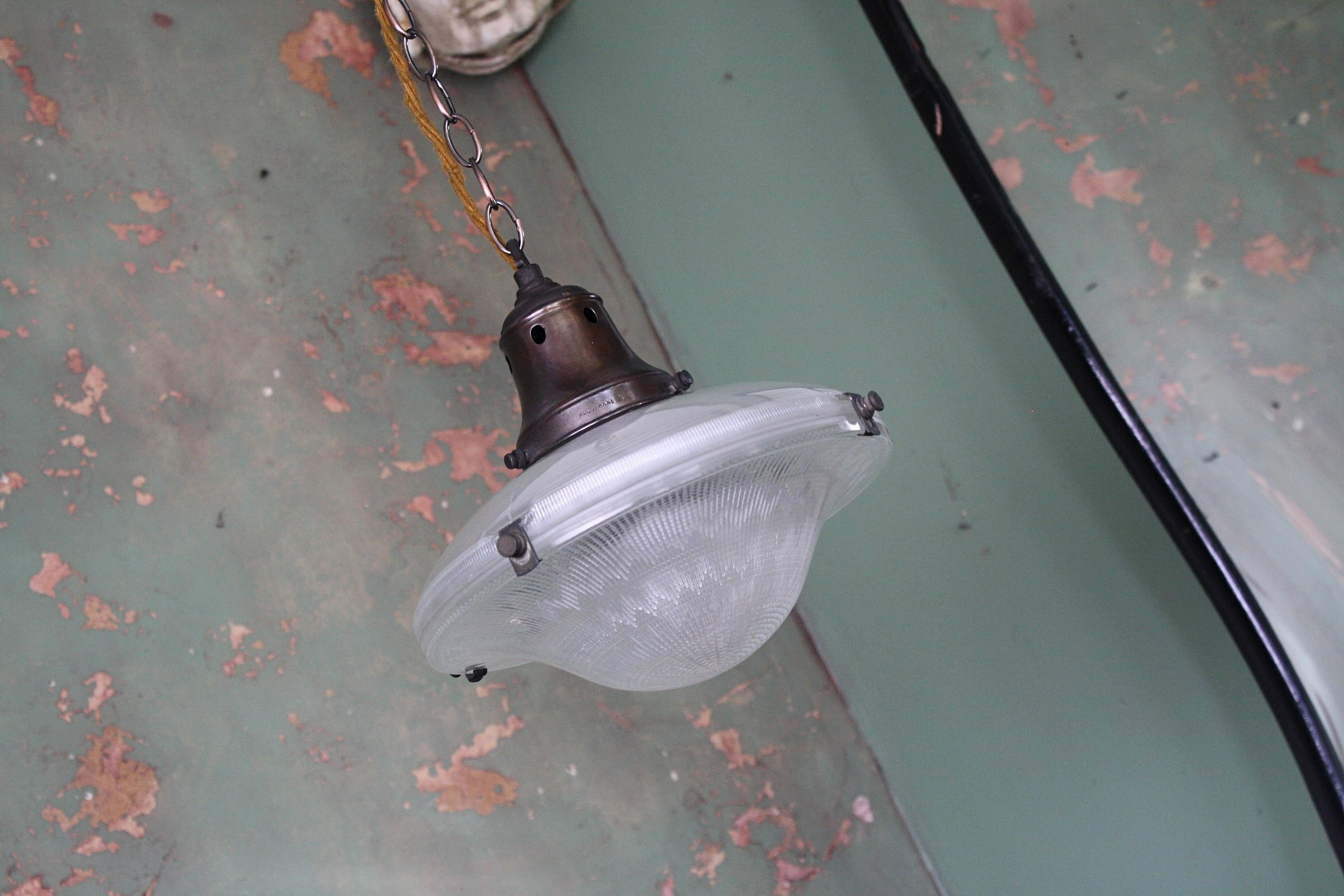 A small two part Holophane flying saucer, prismatic glass with original Holophane bronze gallery and clips. 

Both sections of glass are in good condition, all metal section have age related oxidation

The light comes with a length of antique