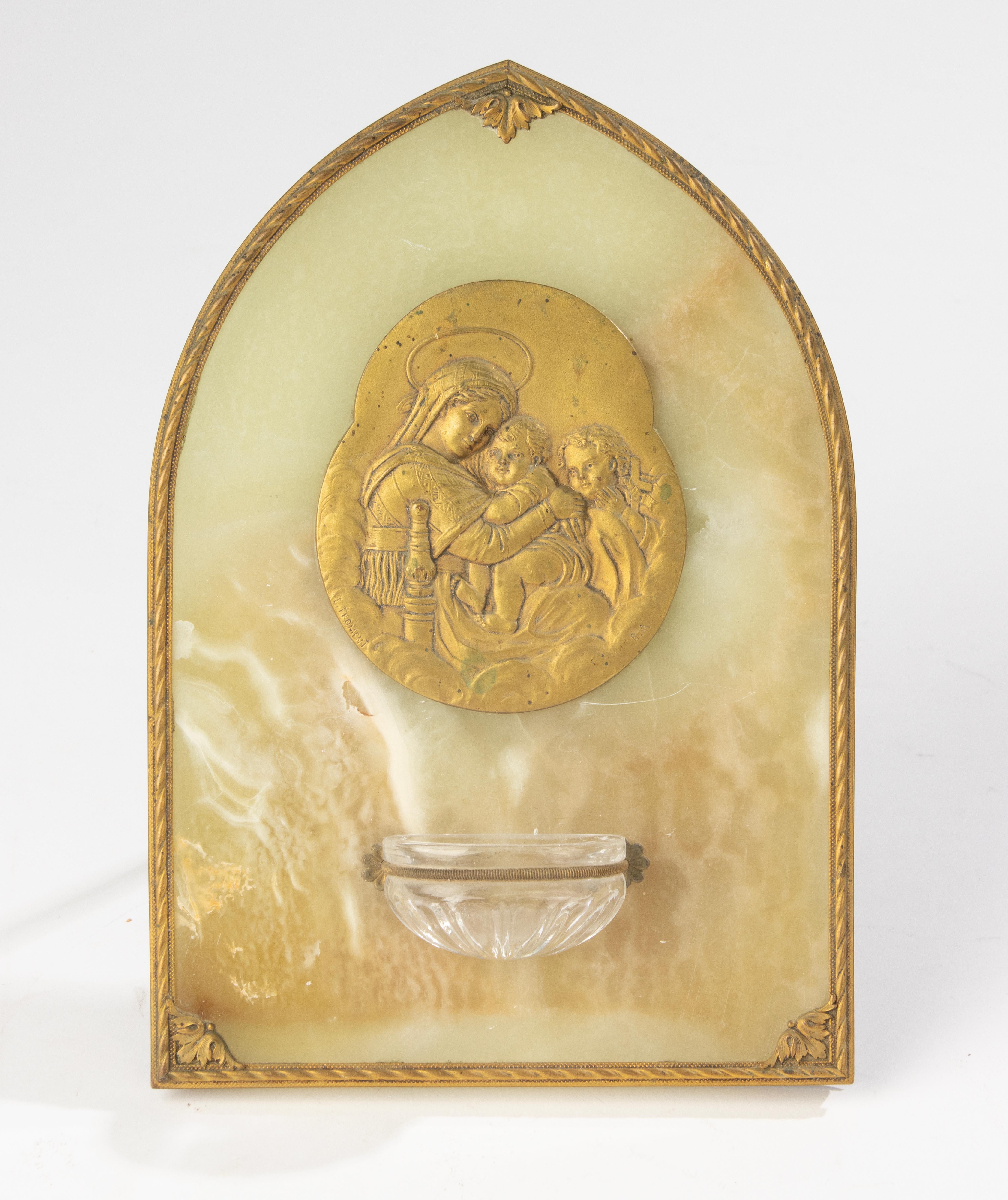Elegant bénitier français datant des années 1900-1910, en onyx richement veiné, orné d'un relief en bronze doré représentant la Vierge à l'Enfant, et muni d'un bassin en cristal finement taillé. Le cadre est orné de montures décoratives en bronze