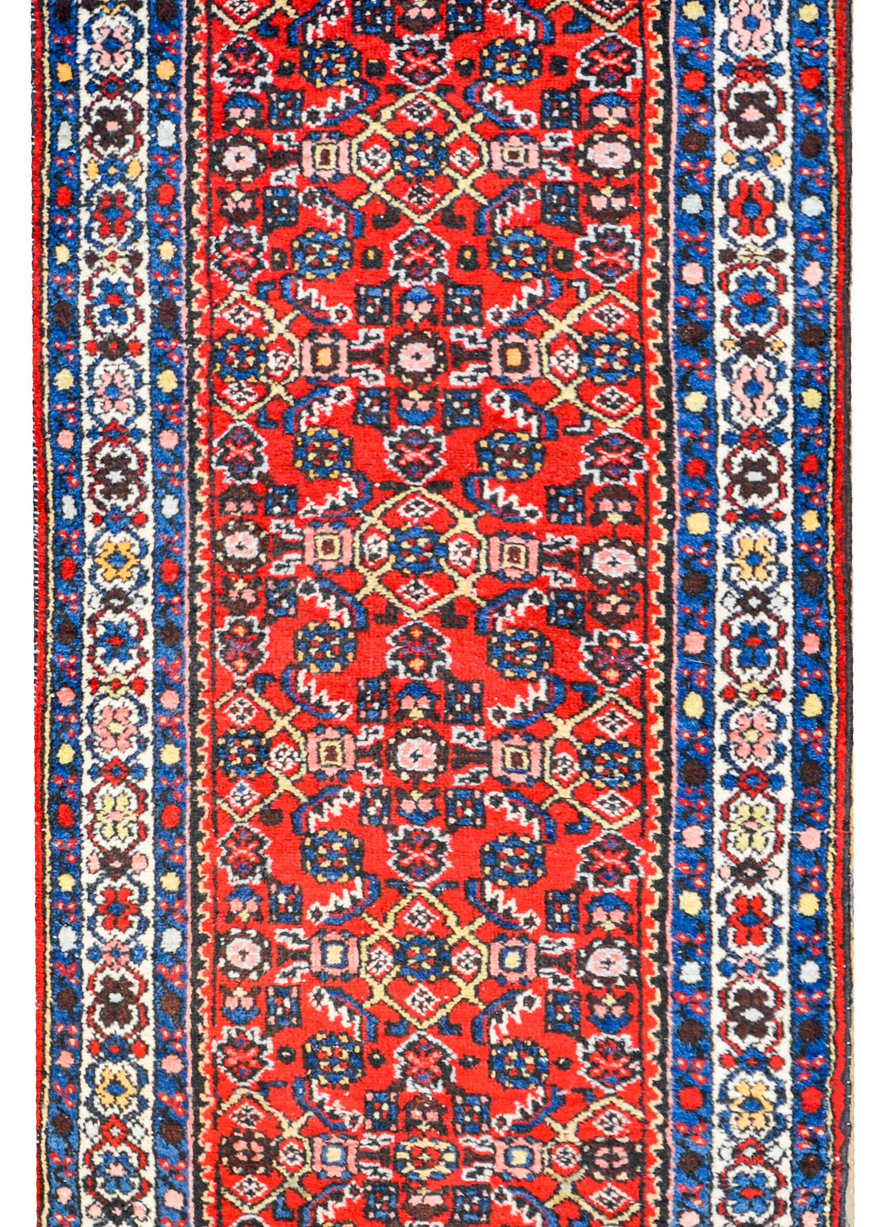 An early 20th century Persian Hosseinabad runner with a fantastic all-over trellis floral and fish patterned field woven in light and dark indigo, gold, white, and green colored vegetable dyed wool, on a bold crimson background. The border is