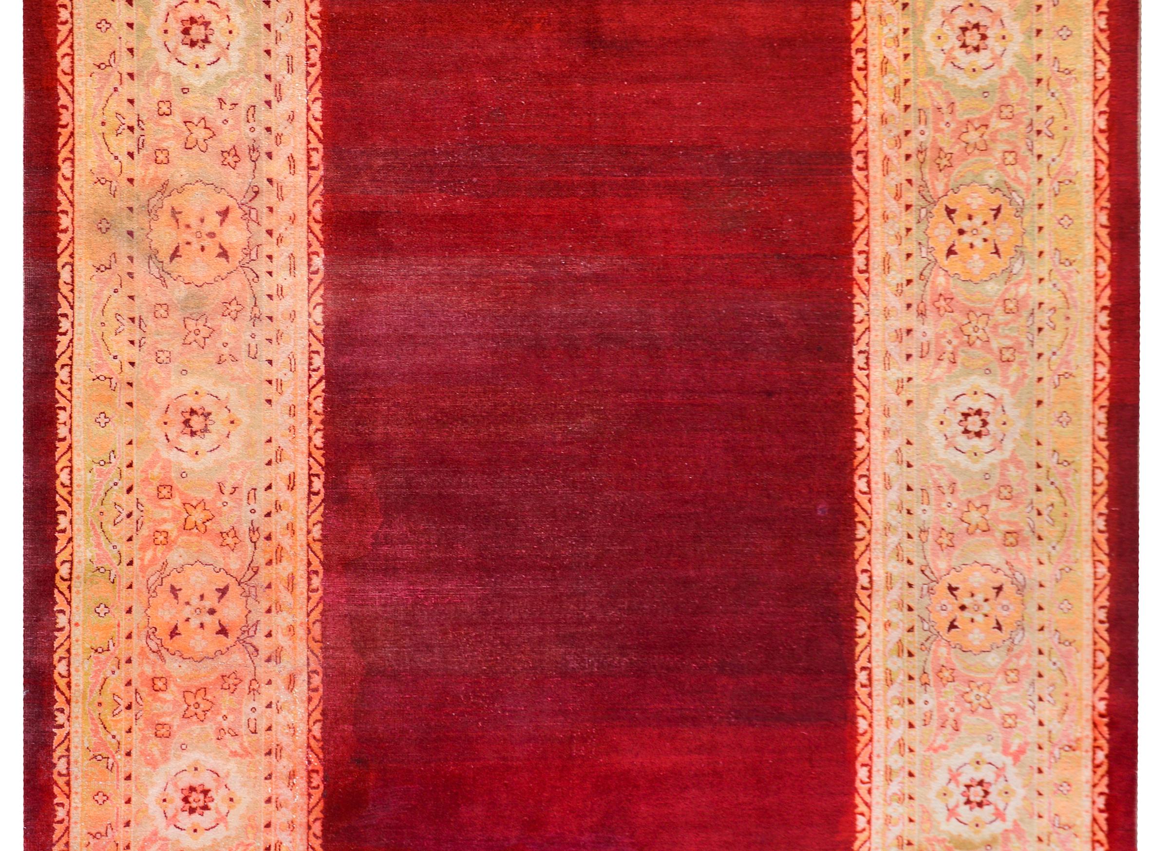 Un bellissimo tappeto indiano Agra dell'inizio del XX secolo con un campo abrasivo color cremisi circondato da un ampio bordo floreale a macchie tessuto in verde chiaro, oro, arancione e rosa.