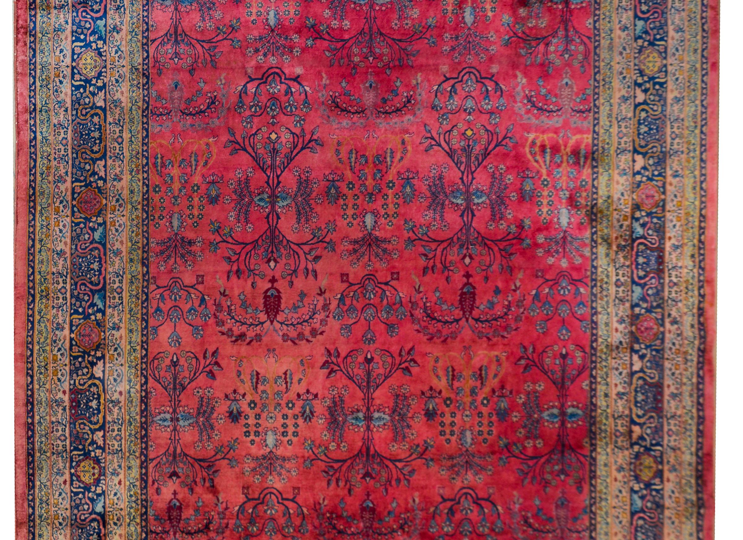 A stunning early 20th century Indian Larestan rug with a whisky floral and vine pattern woven in light and dark indigo, cream, and pink set against an abrash fuchsia background. The border is complex with multiple narrow borders with petite floral