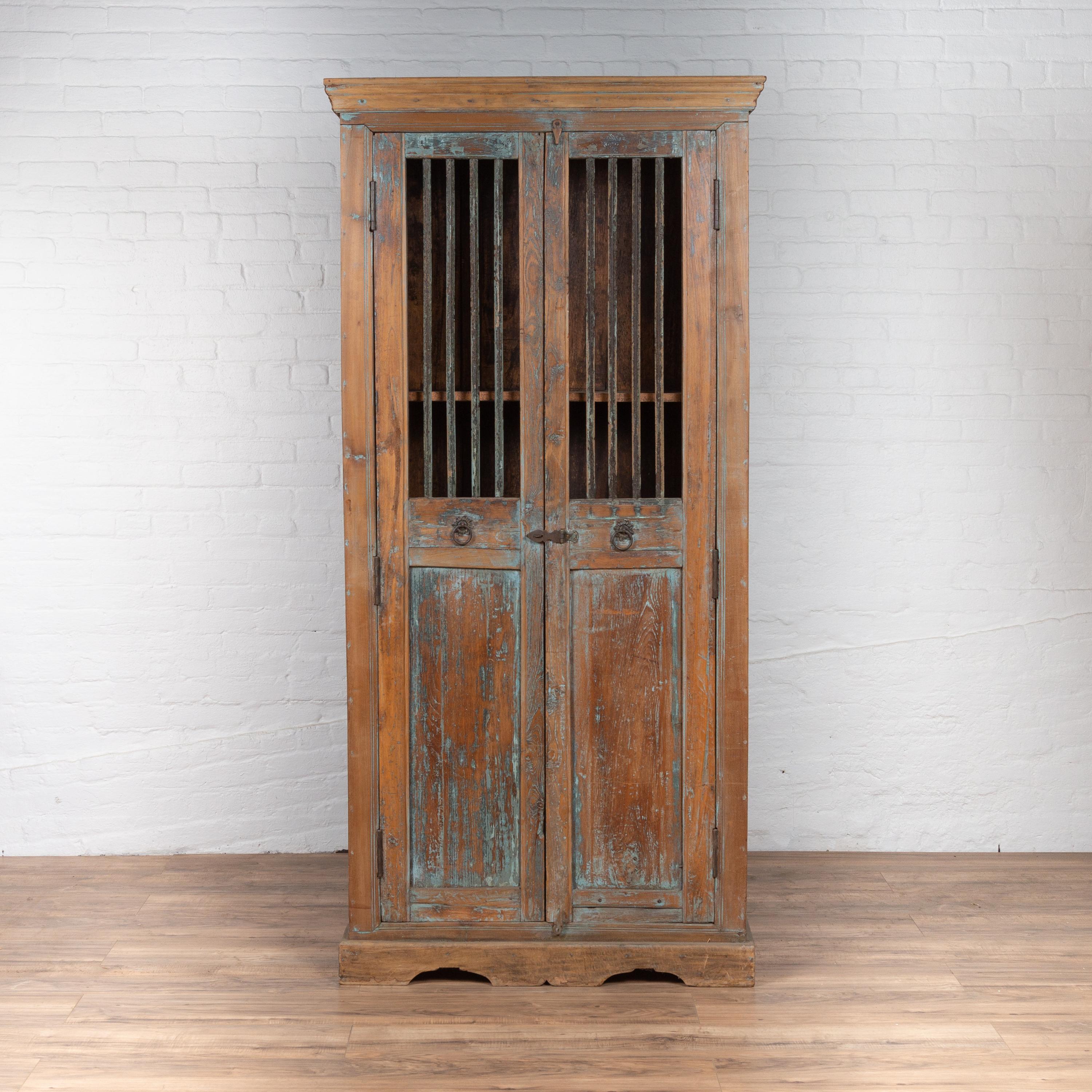 An Indian antique wooden kitchen cabinet from the early 20th century with distressed finish and slatted doors. Born in India during the early years of the 20th century, this charming kitchen cabinet features a molded cornice sitting above two tall