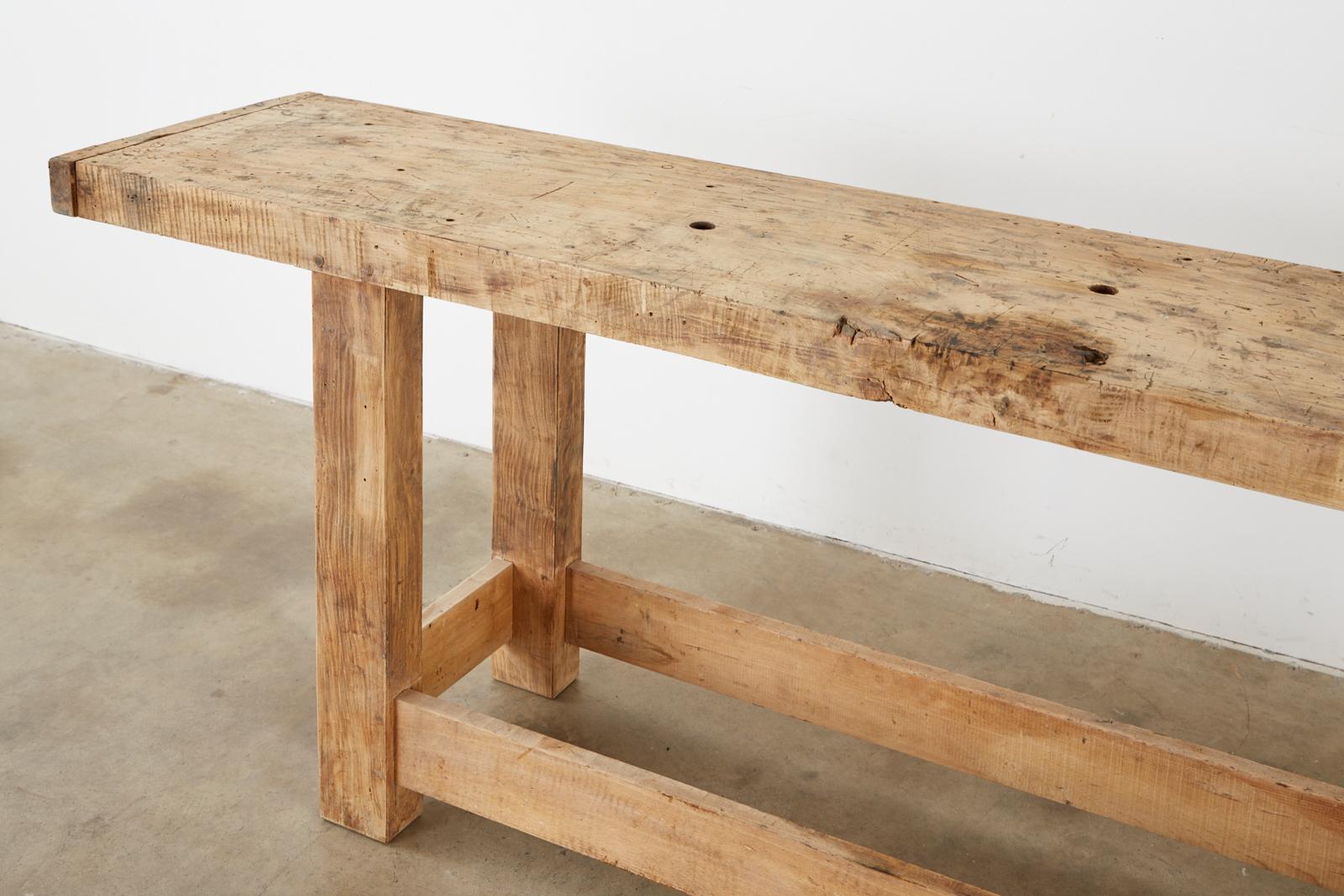 Repurposed early 20th century industrial style carpenter's workbench. Crafted from a large wood timber that appears to be walnut. The massive top features a 3 inch thick solid plank with breadboard ends. Supported by thick, square legs conjoined by