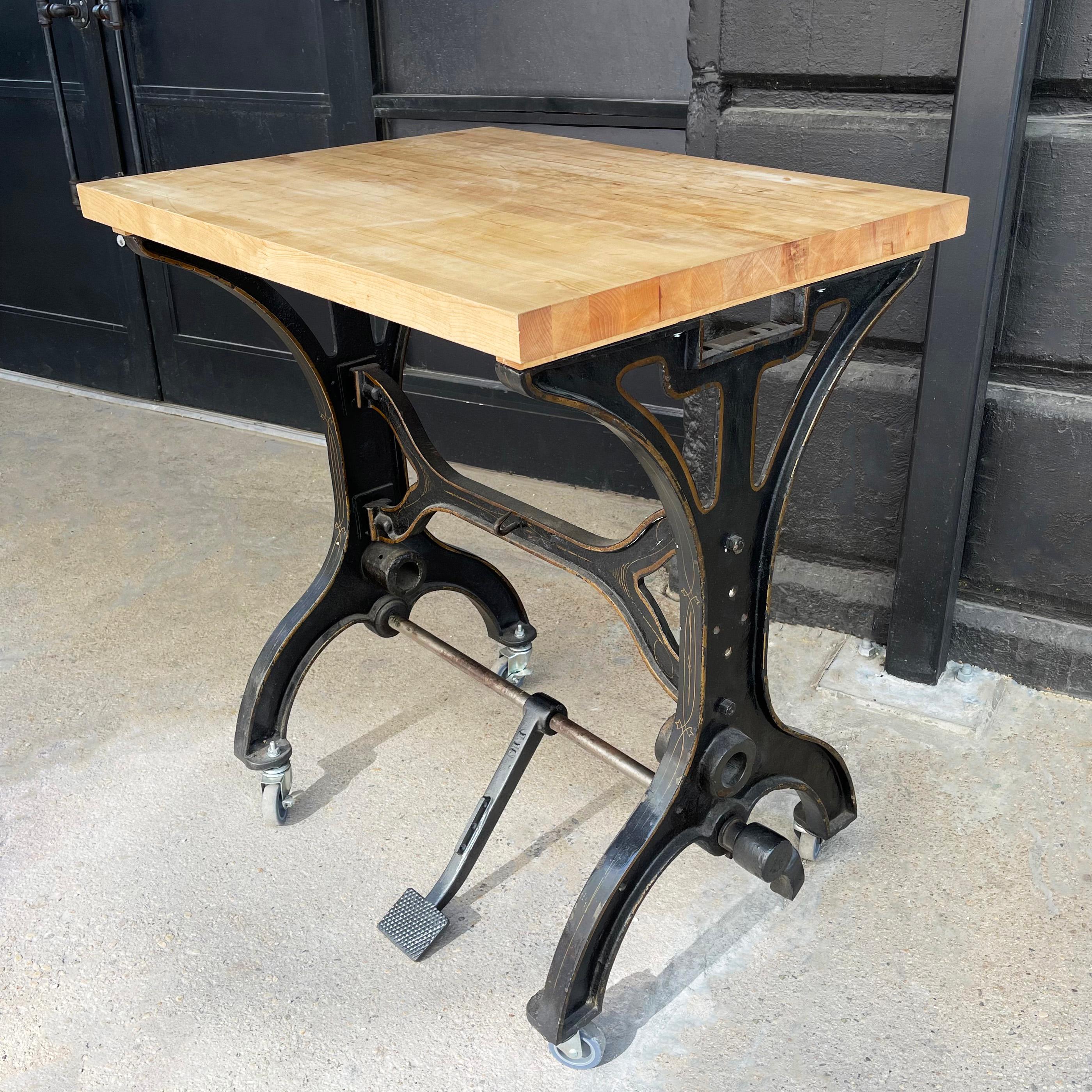 Turn of the 20th century, tall, industrial table features a japanned, cast iron machine base with brass toned filigree details with natural maple butcher block top. The table rolls on casters that are removeable lowering the table by 4 inches.