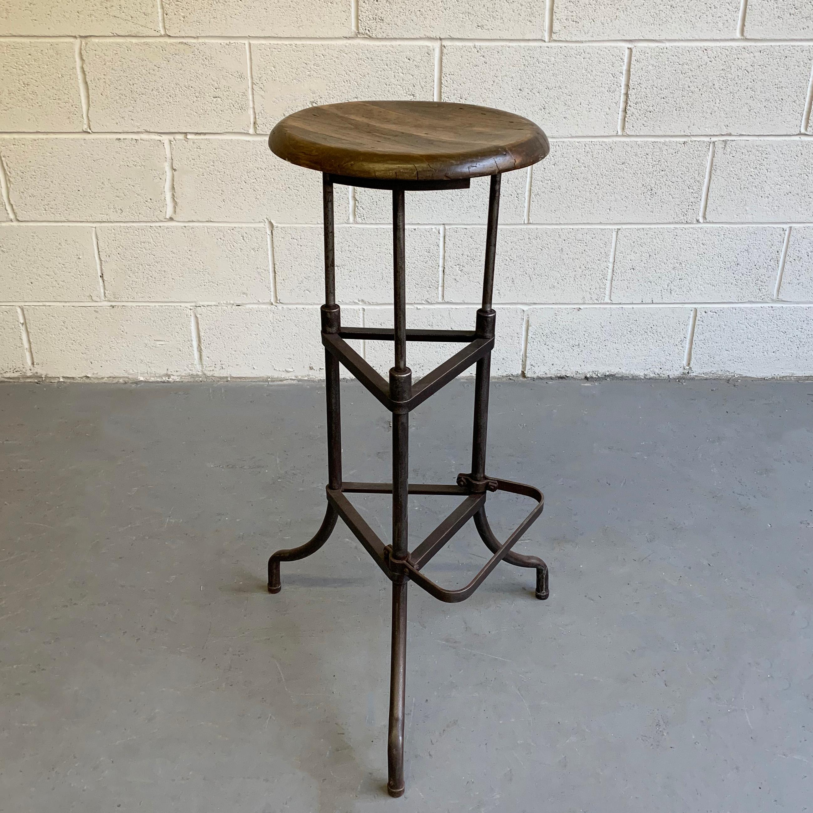 Industrial, early 20th century, drafting stool features a tripod, brushed steel base with footrest and 14 inch diameter, maple seat. Footrest is 11 inches wide and 11.5 inches from the floor.