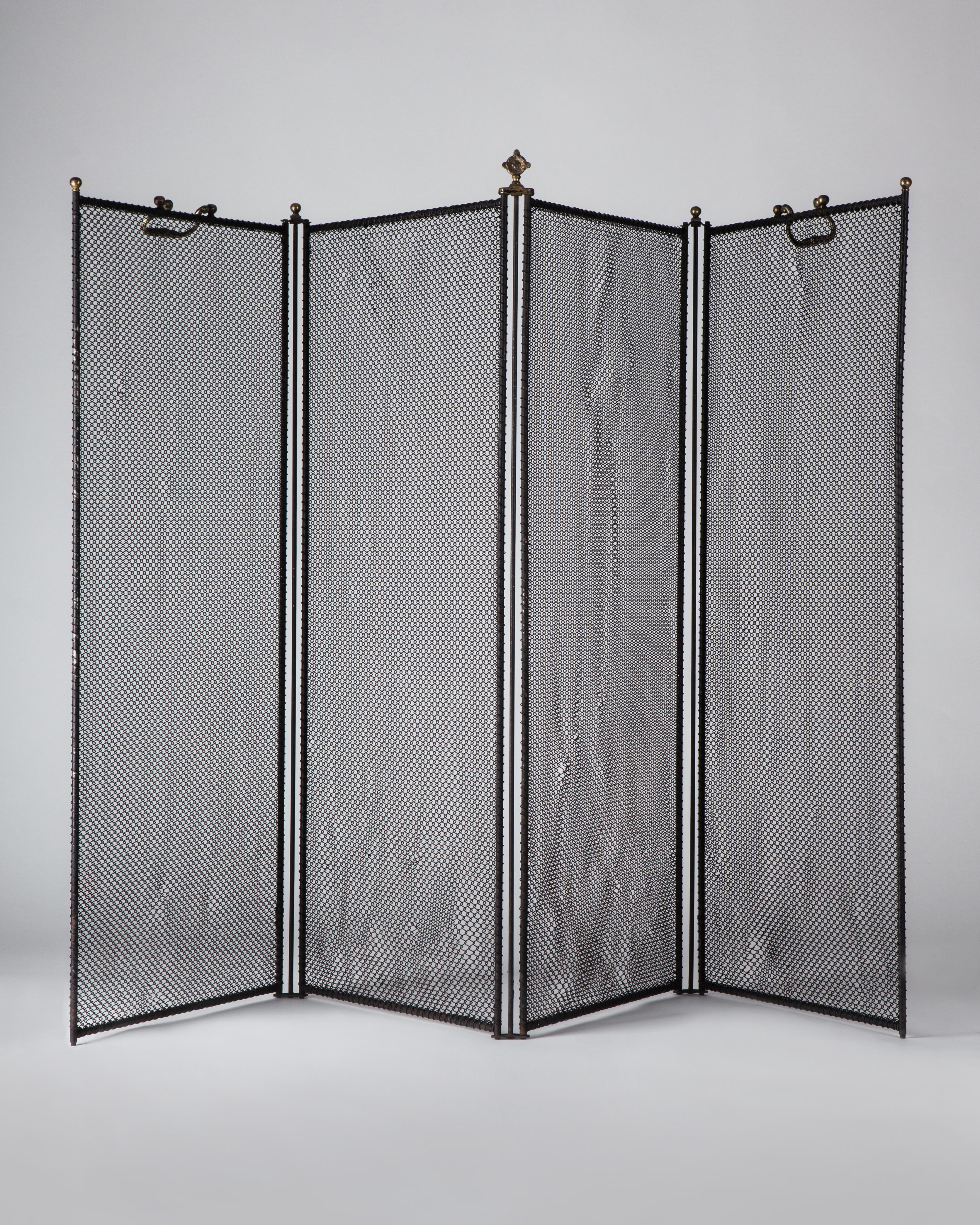 A blackened iron, wire cloth four-panel folding fire screen with aged brass handles and finials, circa 1920.

Dimensions:
Overall (extended) 32