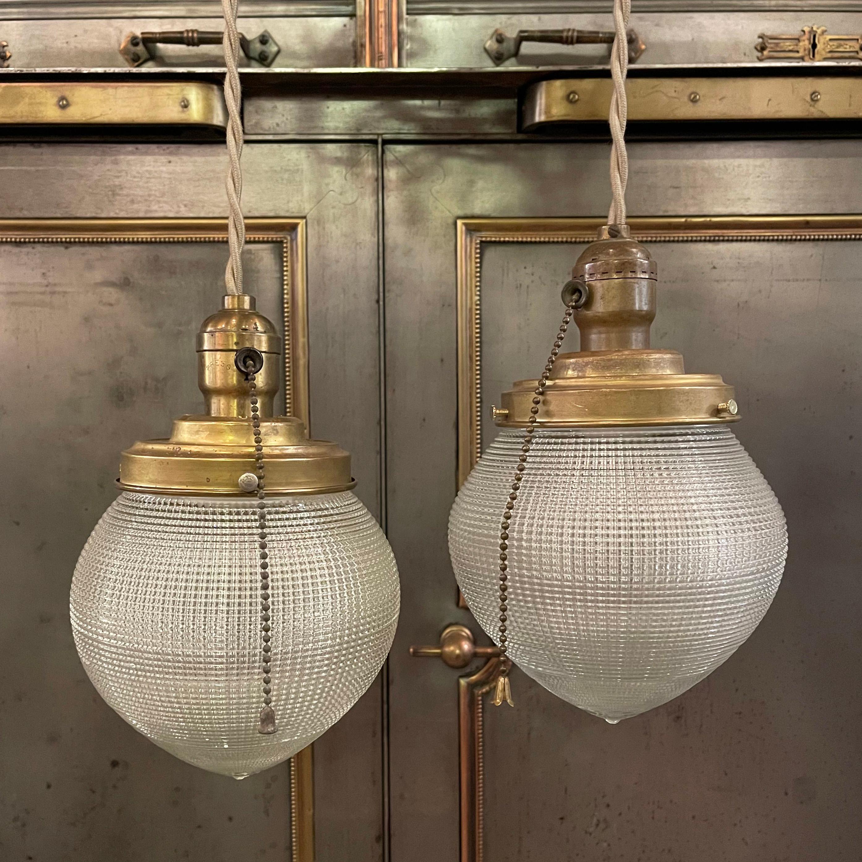 Pair of early 20th century, industrial pendant lights with acorn shape, prismatic, Holophane glass shades and brass hardware with pull chains are newly wired with 48 inches of beige braided cloth cord. Sold as a pair.
