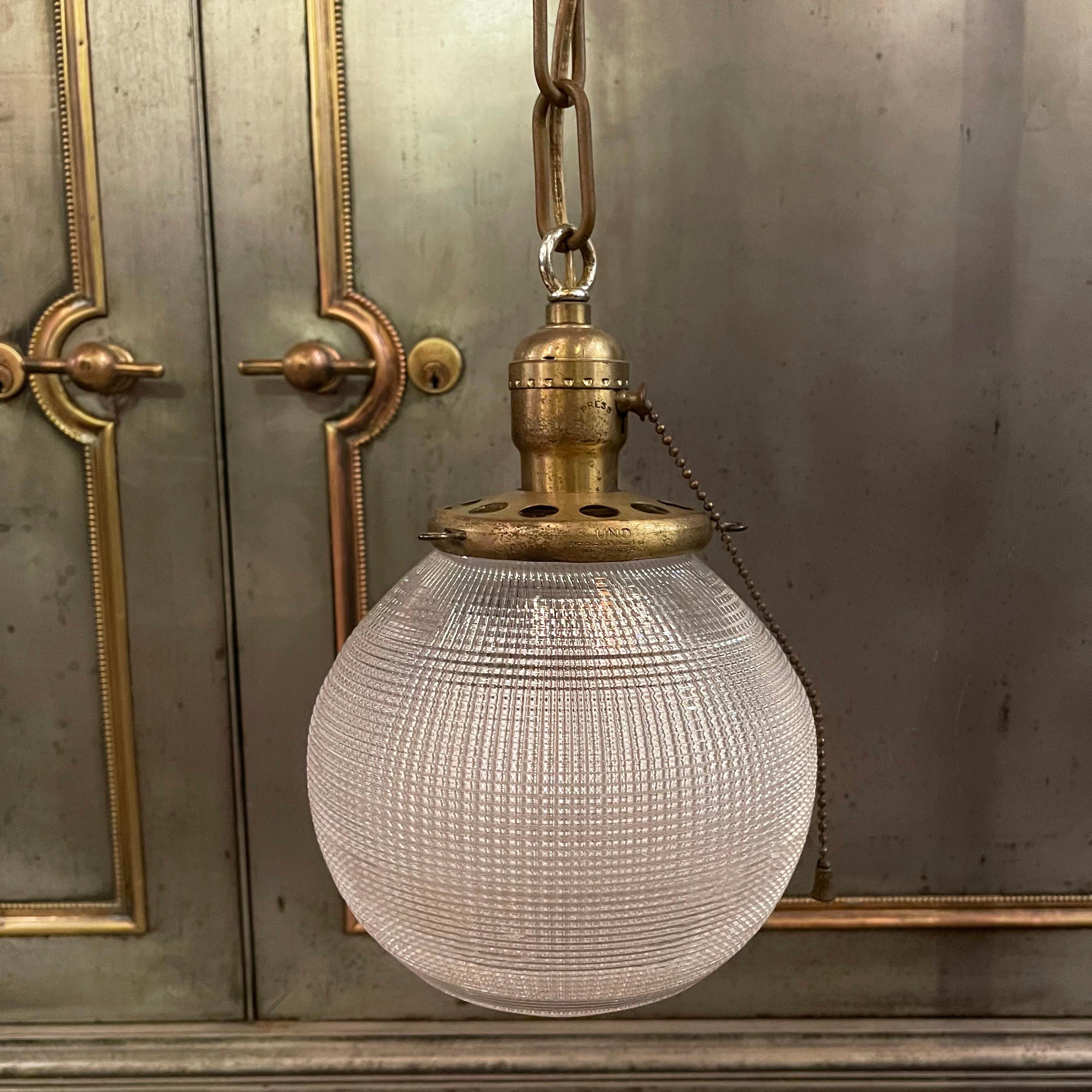 Early 20th century, industrial pendant light with a prismatic Holophane glass globe shade and brass pull chain fitter, chain link and canopy is newly wired to hang at an overall height of 25 inches.