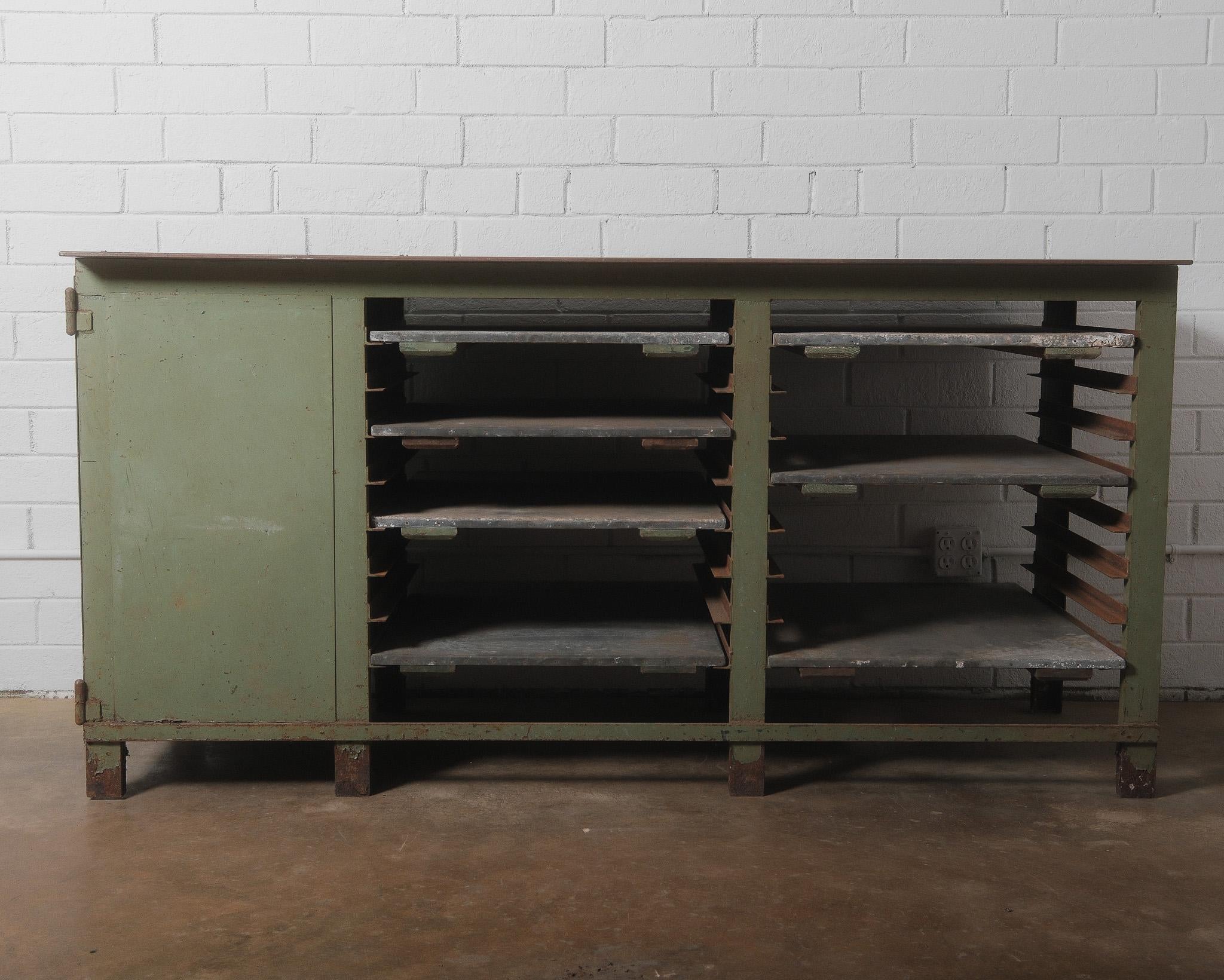 Questo banco da lavoro industriale in metallo dell'inizio del XX secolo è un esempio straordinario di artigianato utilitaristico. Costruito interamente in acciaio, presenta un piano arrugginito fortemente patinato, un corpo verniciato in verde con