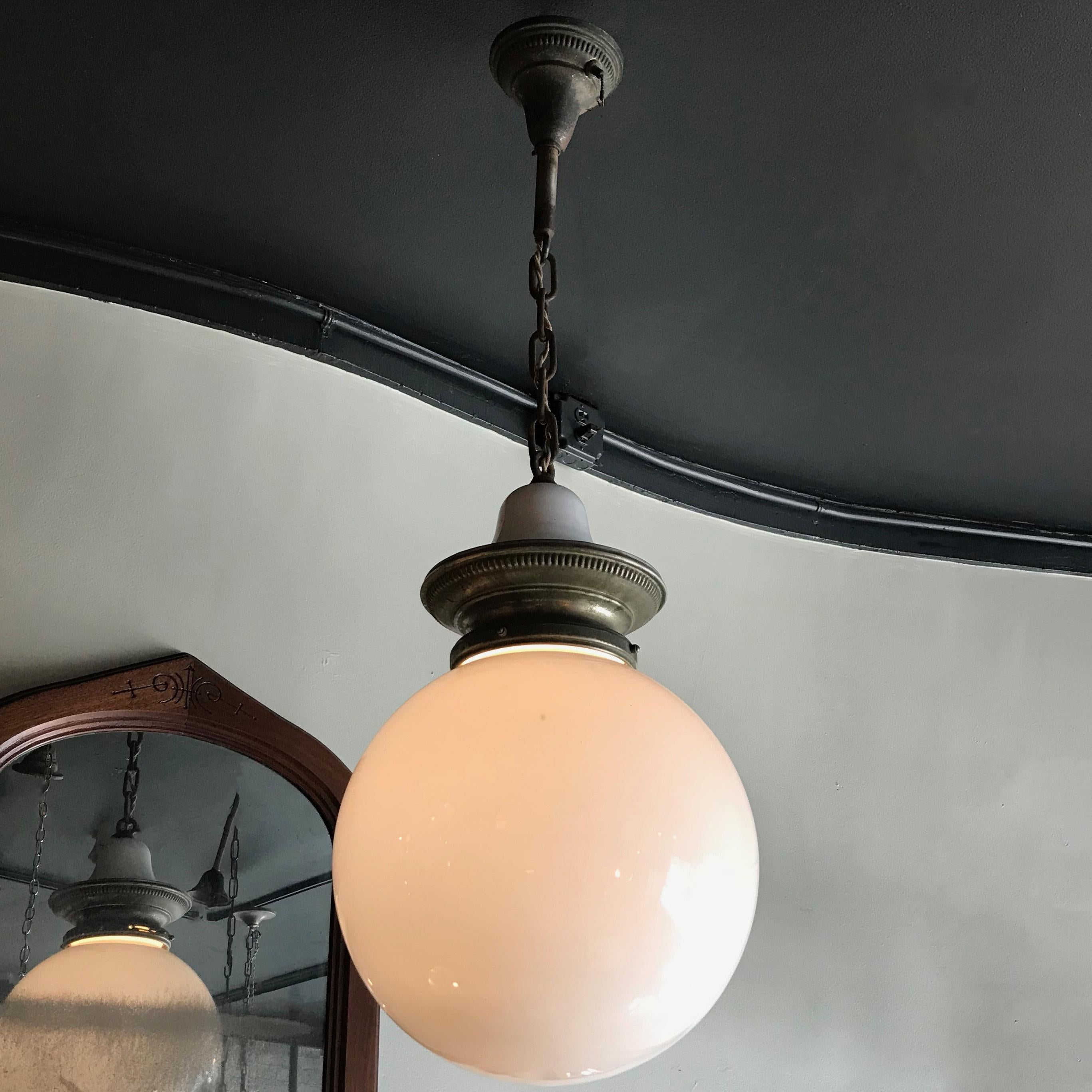 Early 20th century, industrial, library pendant light features a 14 inch milk glass globe shade with nickel-plated brass and porcelain enameled crown fitter, brass chain and canopy is wired to accept up to a 300 watt bulb. The overall height is 43
