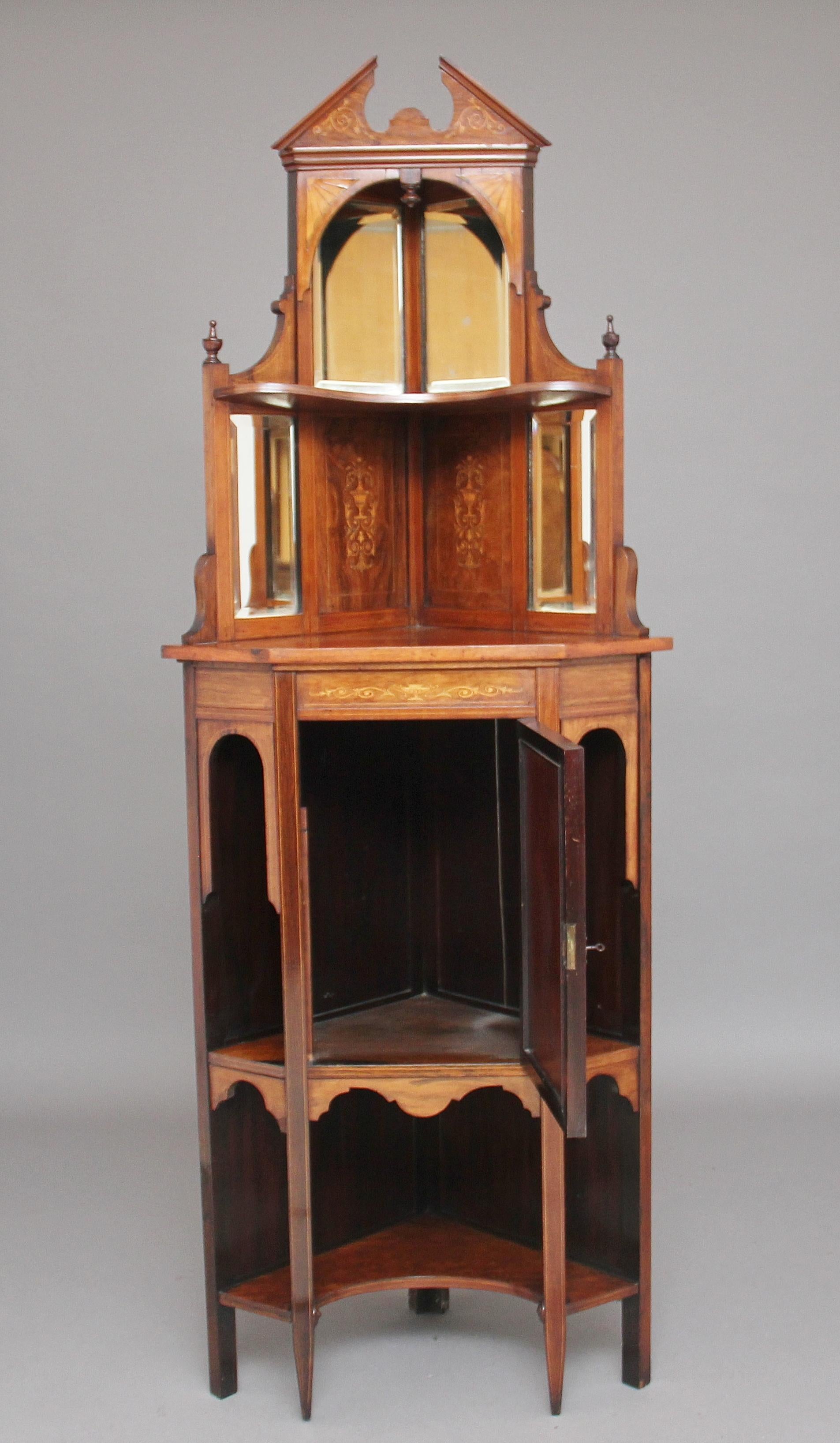 An early 20th century rosewood and marquetry inlaid standing corner cabinet, the broken arched pediment above a mirrored back, the central cupboard door inlaid with swags and bows above an urn, standing on square tapered legs, circa 1910.