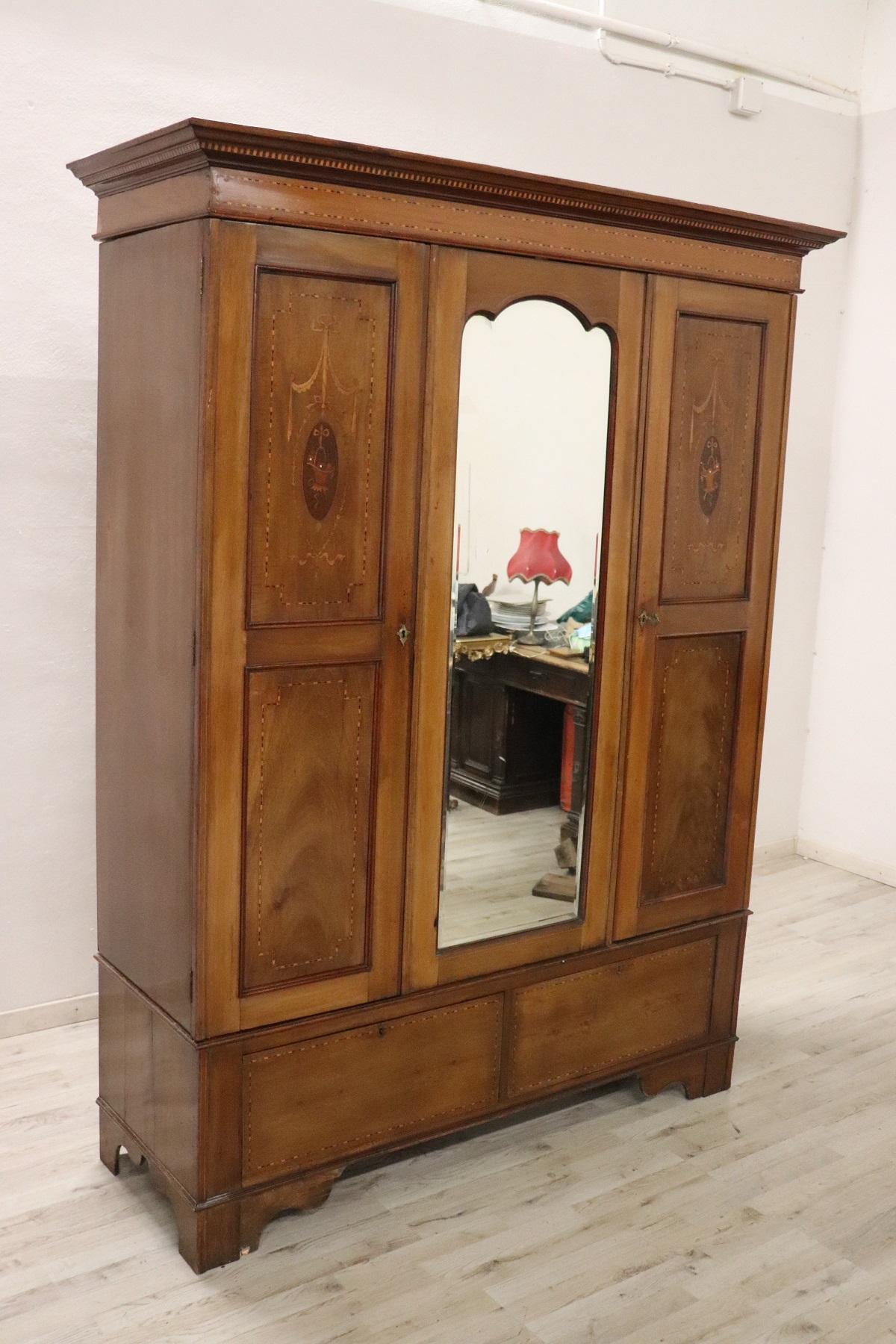 Rare and important antique wardrobe in solid walnut wood made in early 20th century. The line is simple and essential, perfect to be placed also in a modern environment. Beautiful patina of walnut wood. Refined wood inlay decoration with floral