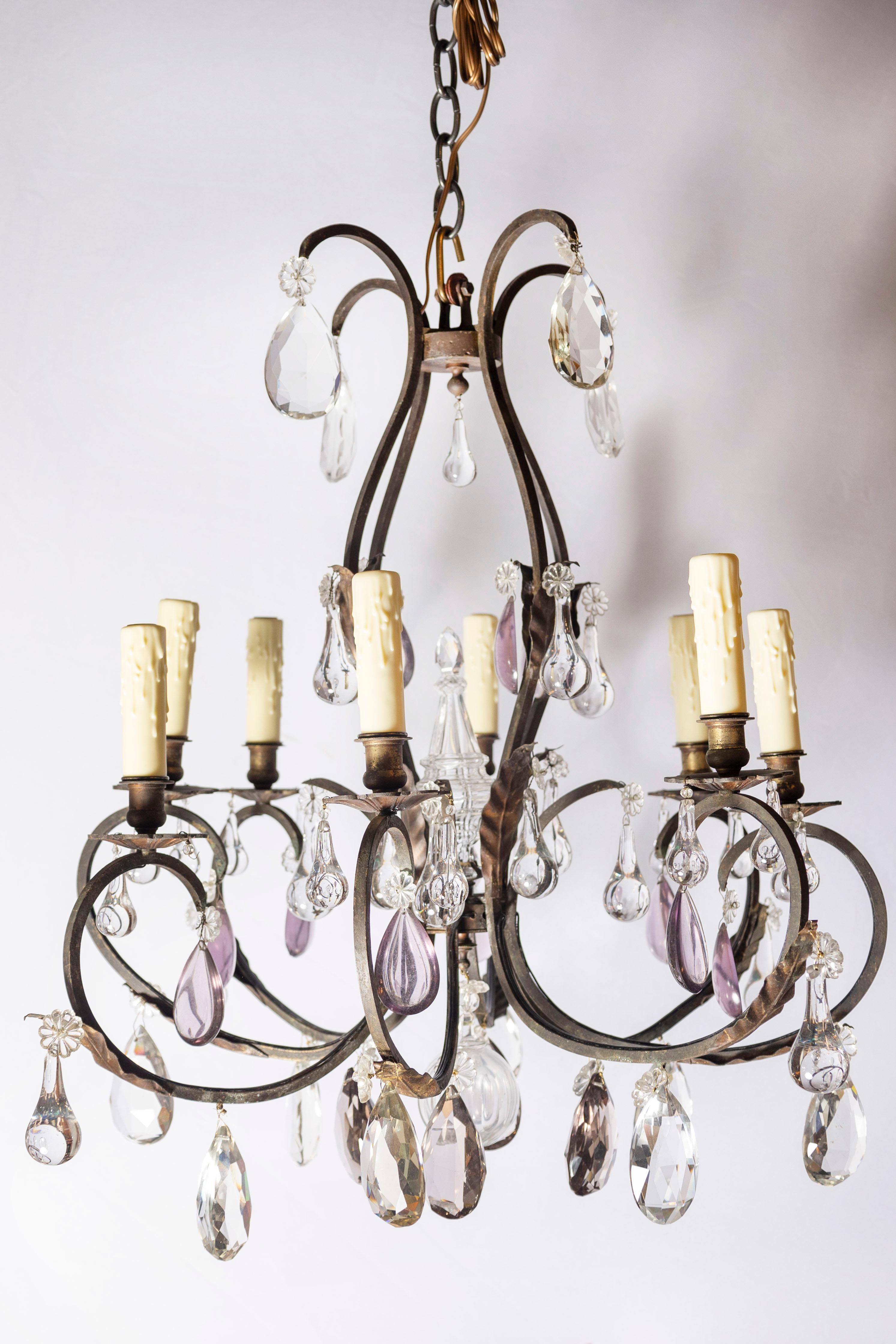 Un'accattivante miscela di eleganza rustica e fascino romantico, questo lampadario francese dell'inizio del XX secolo presenta una scultorea struttura in ferro battuto delicatamente ornata da gocce di cristallo chiaro e ametista. Il design mette in