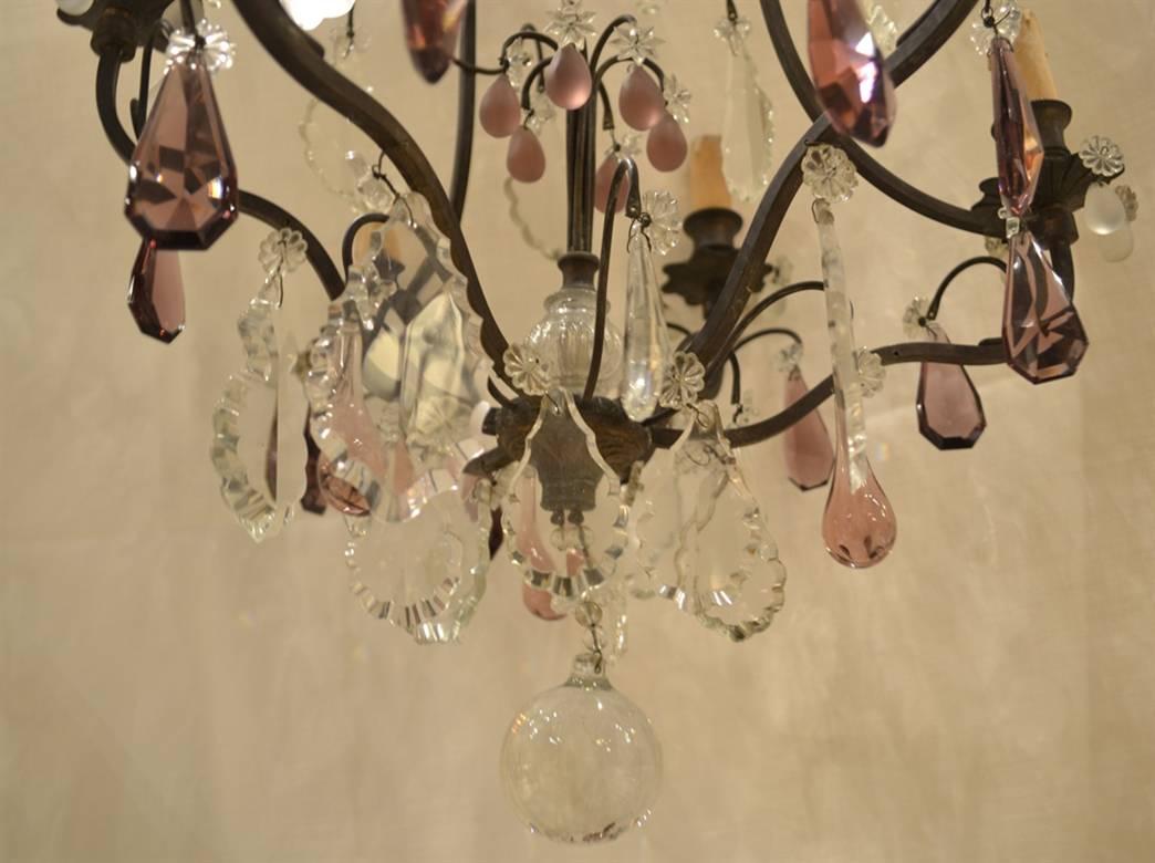 This decorative French chandelier was purchased in Paris. It dates from the early 1900s and features six arms draped with multiple clear crystals and teardrop, lozenge and frosted amethyst crystals. The piece has old candle sleeves, is in very good