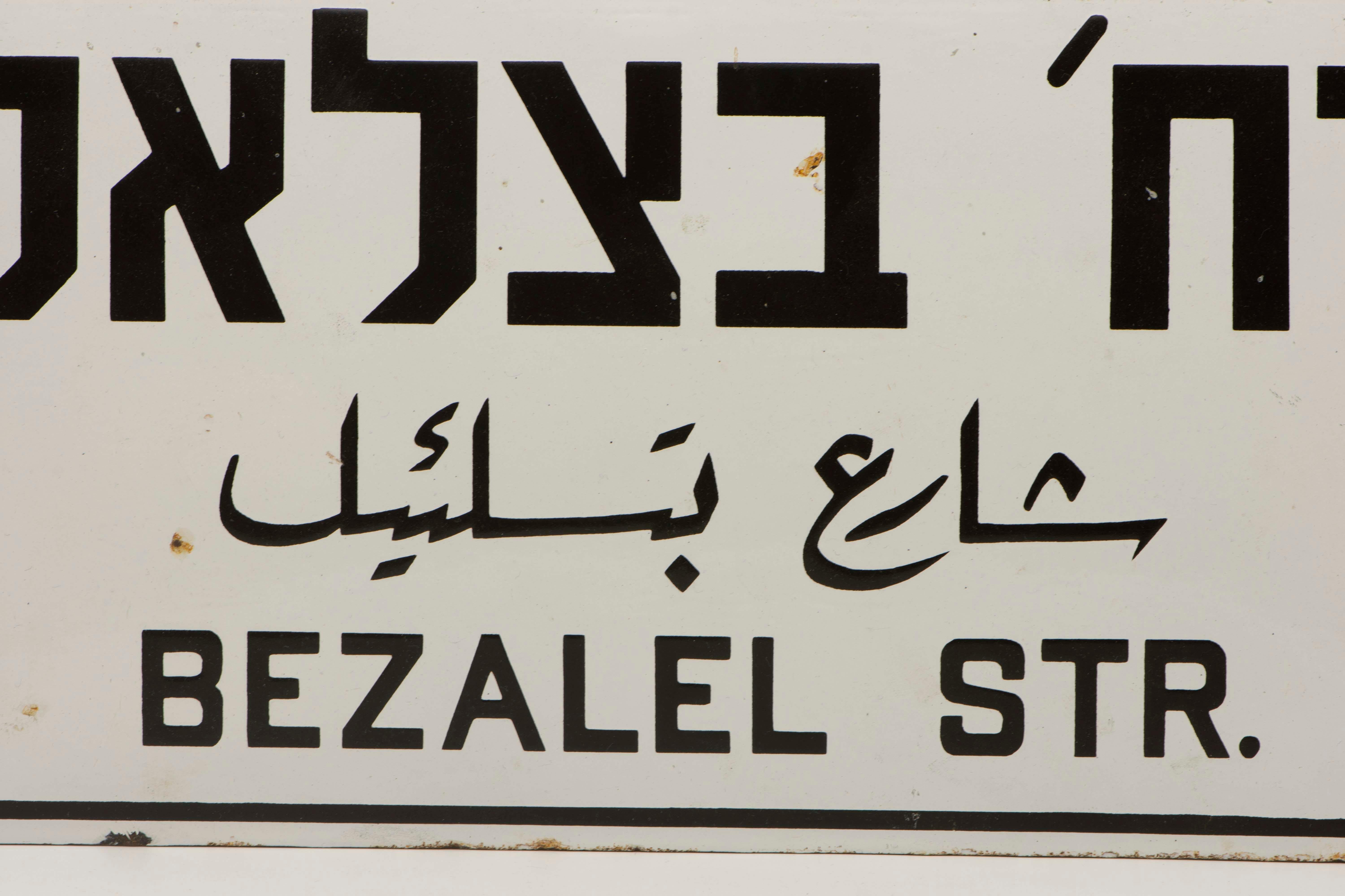 Three languages iron and enamel street sign, circa 1920.
The sign was made to Honor Bezalel who was the chief artisan of the Tabernacle and was in charge of building the Ark of the Covenant, assisted by Aholiab.
The three languages indicate the sign