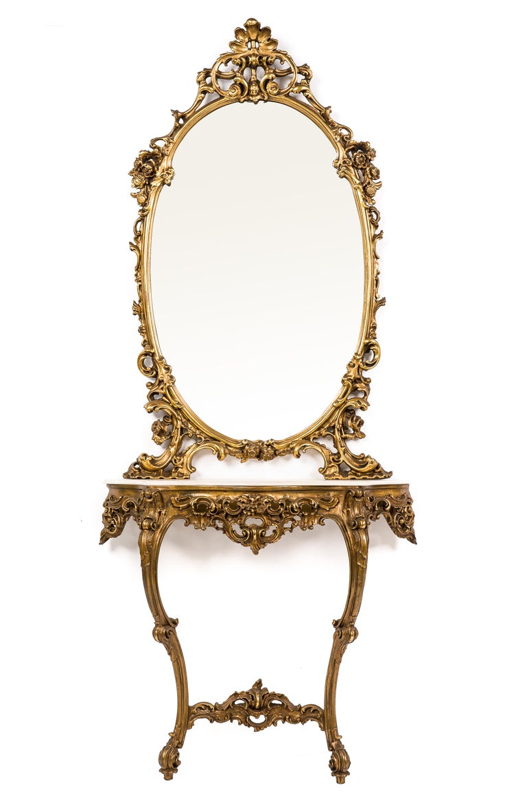 This highly decorative console table with an oval mirror was made in early-20th century Italy. The carved wood table and mirror frame were decorated with delicate flowers, acanthus, shell, and scroll motifs. The symmetrical design and rich