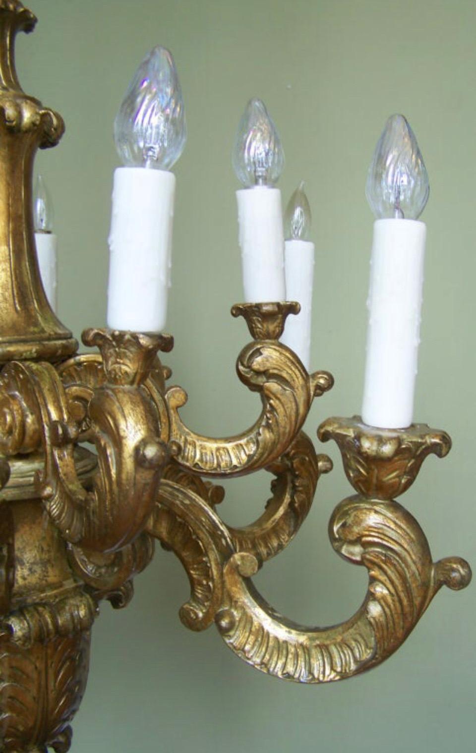 Grand lustre italien du début du XXe siècle en bois doré sculpté à la main comporte douze lampes sur deux étages. Le lustre baroque en bois doré présente une impressionnante tige tournée sculptée à la main descendant à quatre rosettes au-dessus