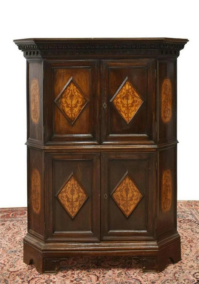 Une armoire d'angle italienne en noyer, corniche moulurée, au-dessus d'un coffret triangulaire, portes d'armoire supérieure et inférieure avec panneaux de marqueterie contrastés, s'ouvrant pour révéler un intérieur à étagères, reposant sur des pieds