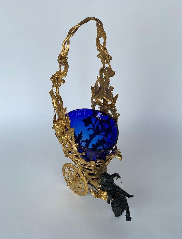 Early 20th century Italian two-tone bronze centerpiece on a gold hue with an overall ornate open work design, accented with a figurative chariot of a putti angel mounted on top of a saddled lion, completed with a graduated cobalt blue glass bowl,