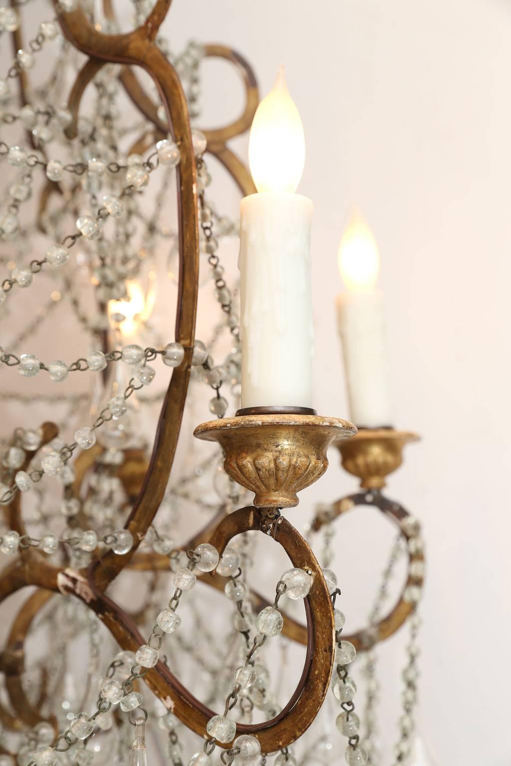 Italian chandelier in wood, gilt-iron and glass. Italian chandelier decorated in hand blown glass pendants, beads and crystal prisms, suspended from an iron and turned wood frame. Wooden elements covered in remnants of gesso. Newly wired for use