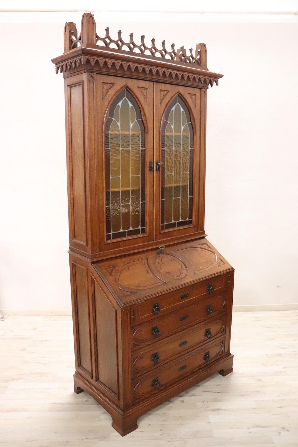 Fantastic Gothic style cabinet made in the first decades of the 20th century. In solid oak wood. Characterized in the upper part by a majestic architectural decoration carved in wood. The two colored cathedral glasses are of great value. This
